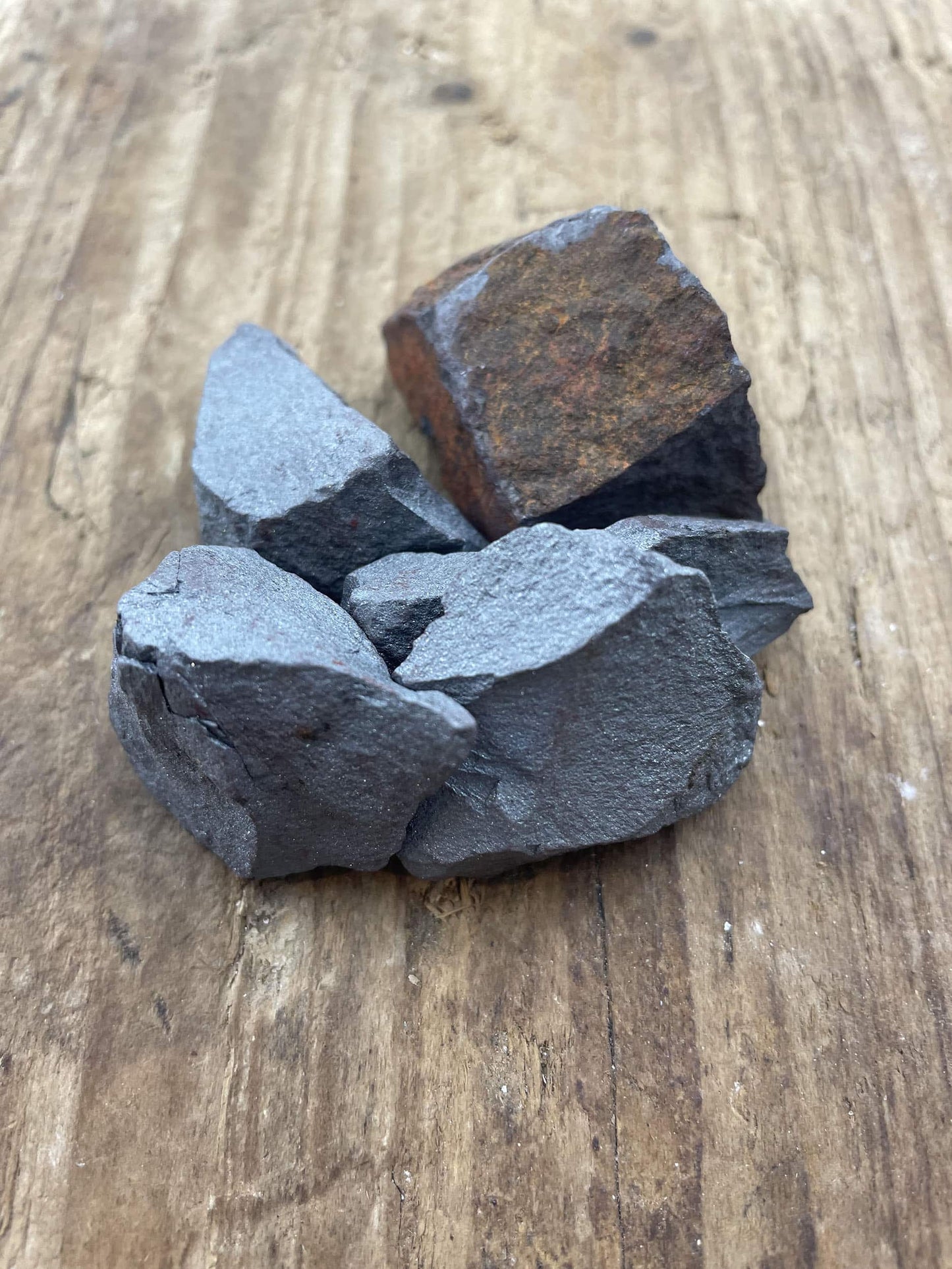 Hæmatit rå (Blodsten) på træoverflade, viser stenens naturlige tekstur og farvevariationer.