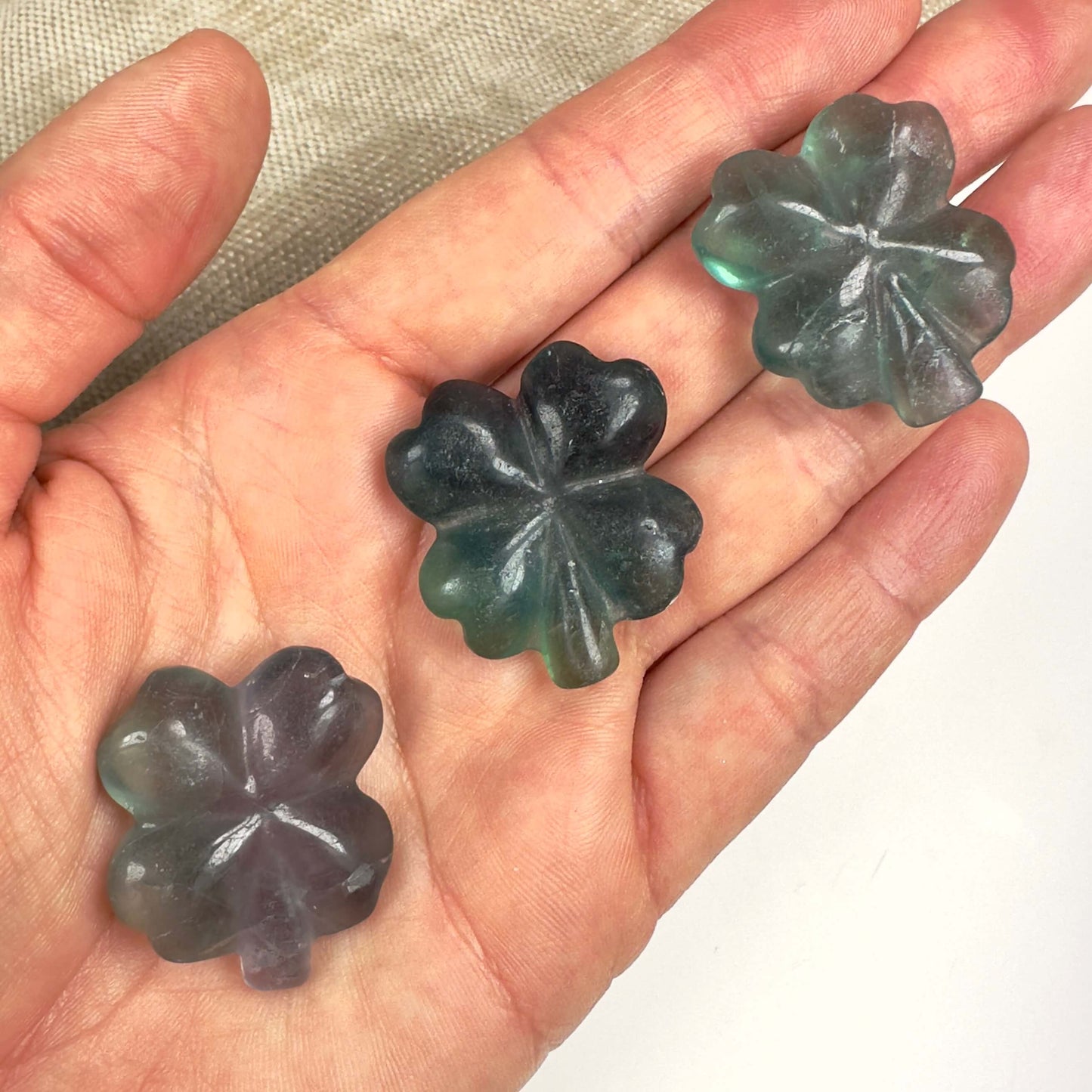 Tre fluorit firkløver i forskellige nuancer af grøn og lilla, der ligger i en åben håndflade.