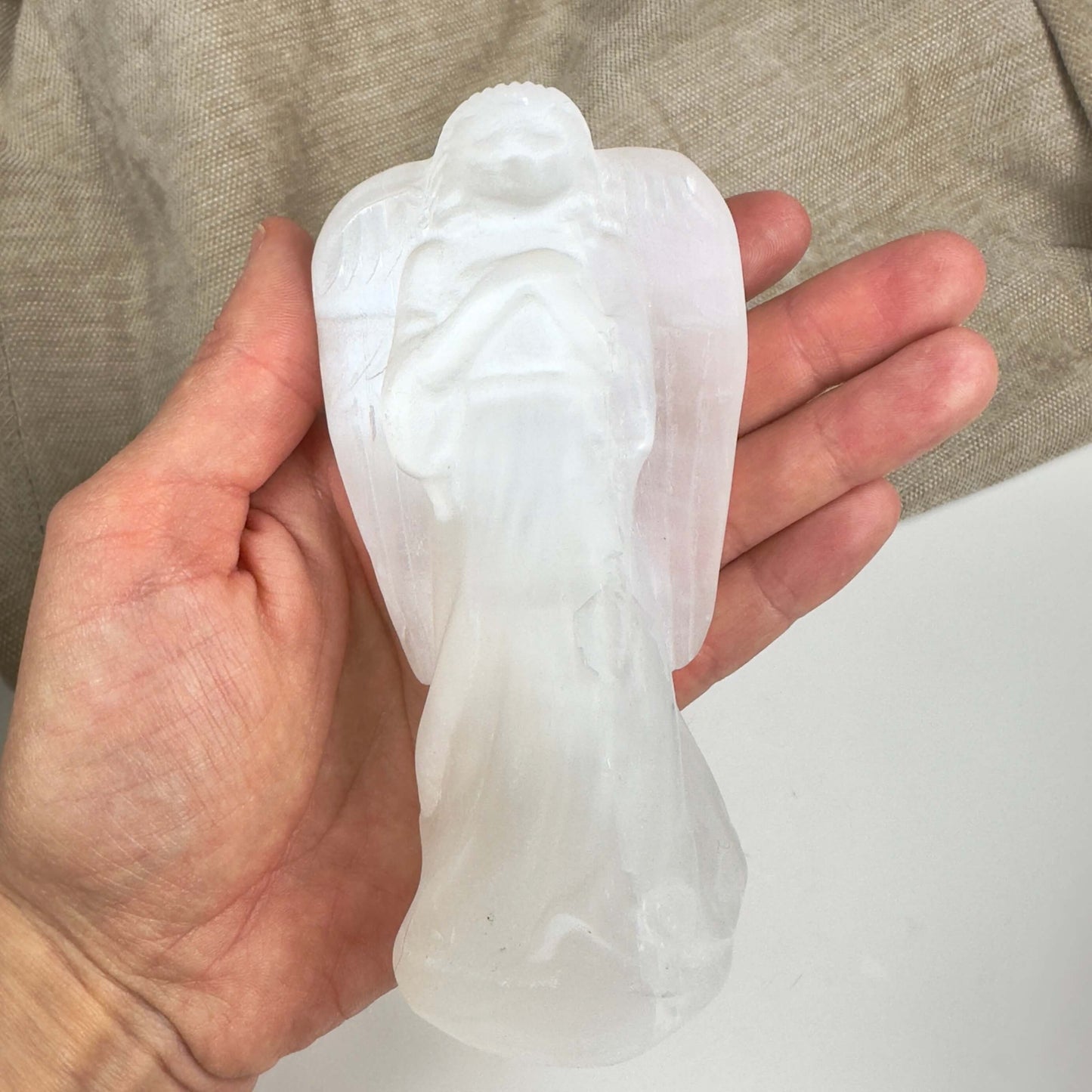 Hånd holder en selenit engel udskåret i hvidt krystal.
