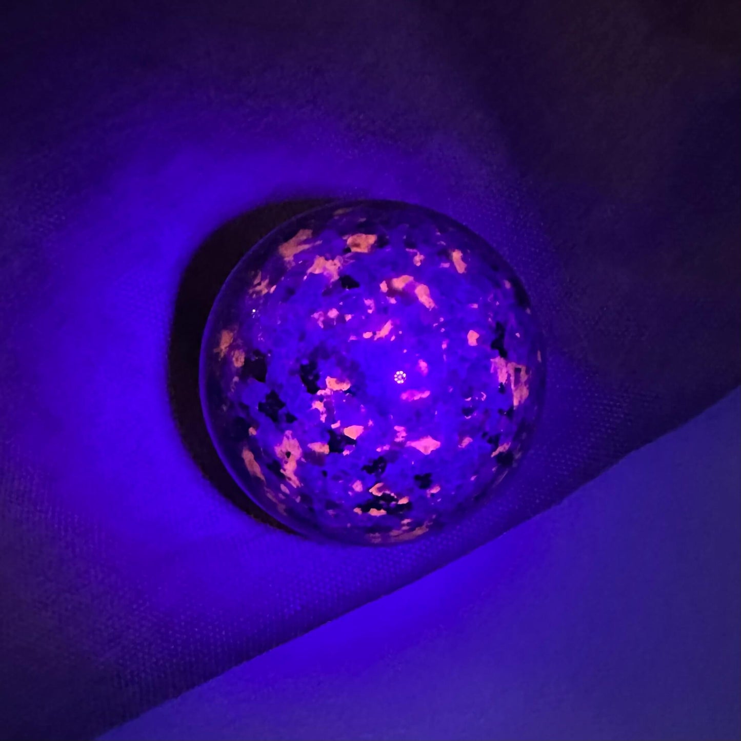 Yooperlit kugle under UV-lys, der fremhæver fluorescerende mønstre i lilla og orange nuancer.