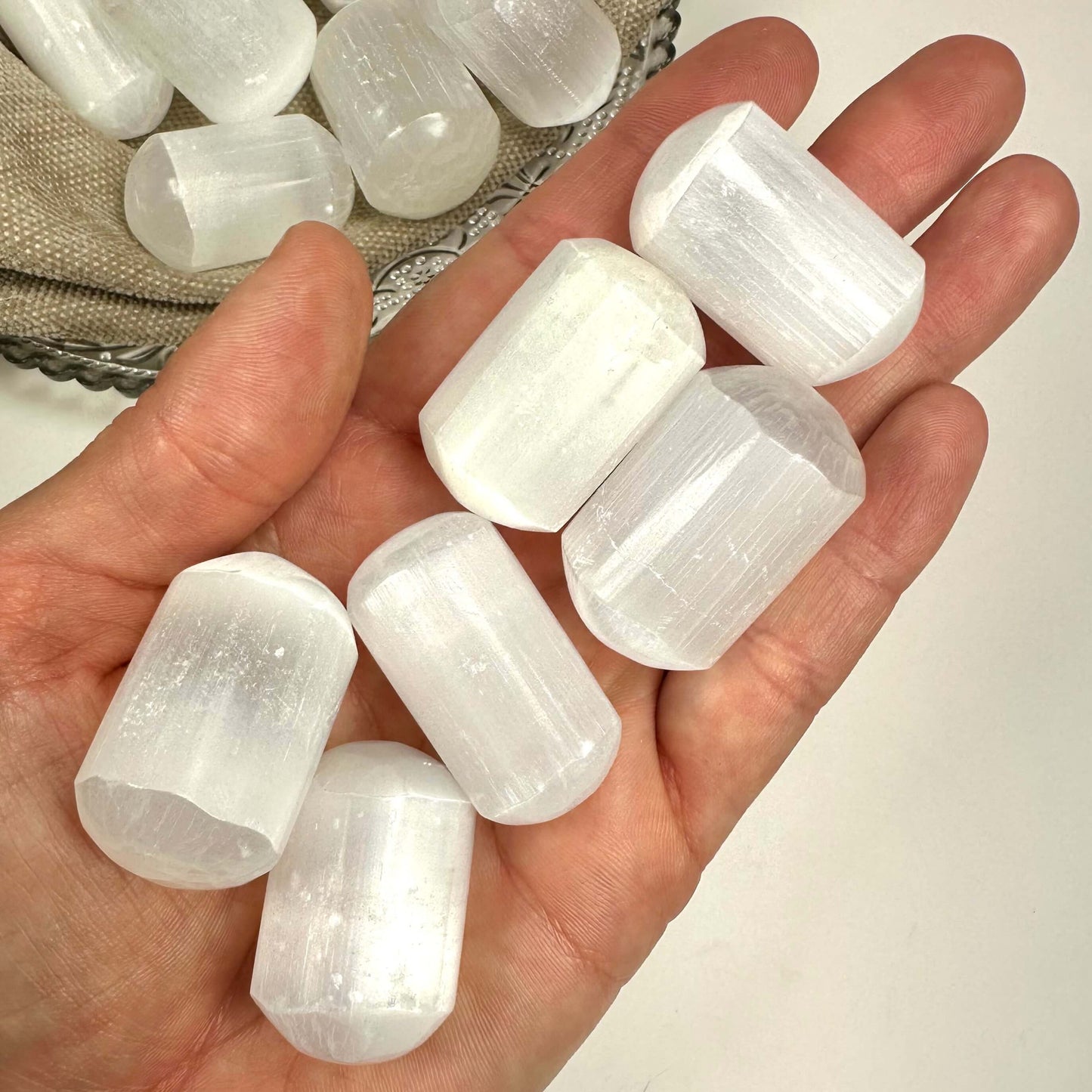 Hånd holder flere hvide selenitcylindre, med flere på en bakke i baggrunden.