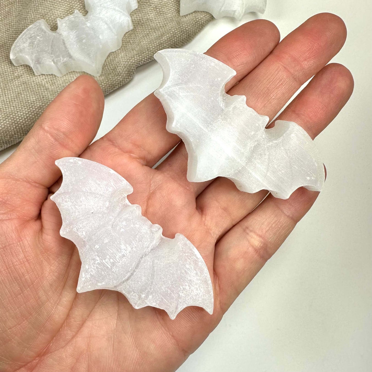 Hånd holder selenit flagermusformede sten på en lys baggrund.
