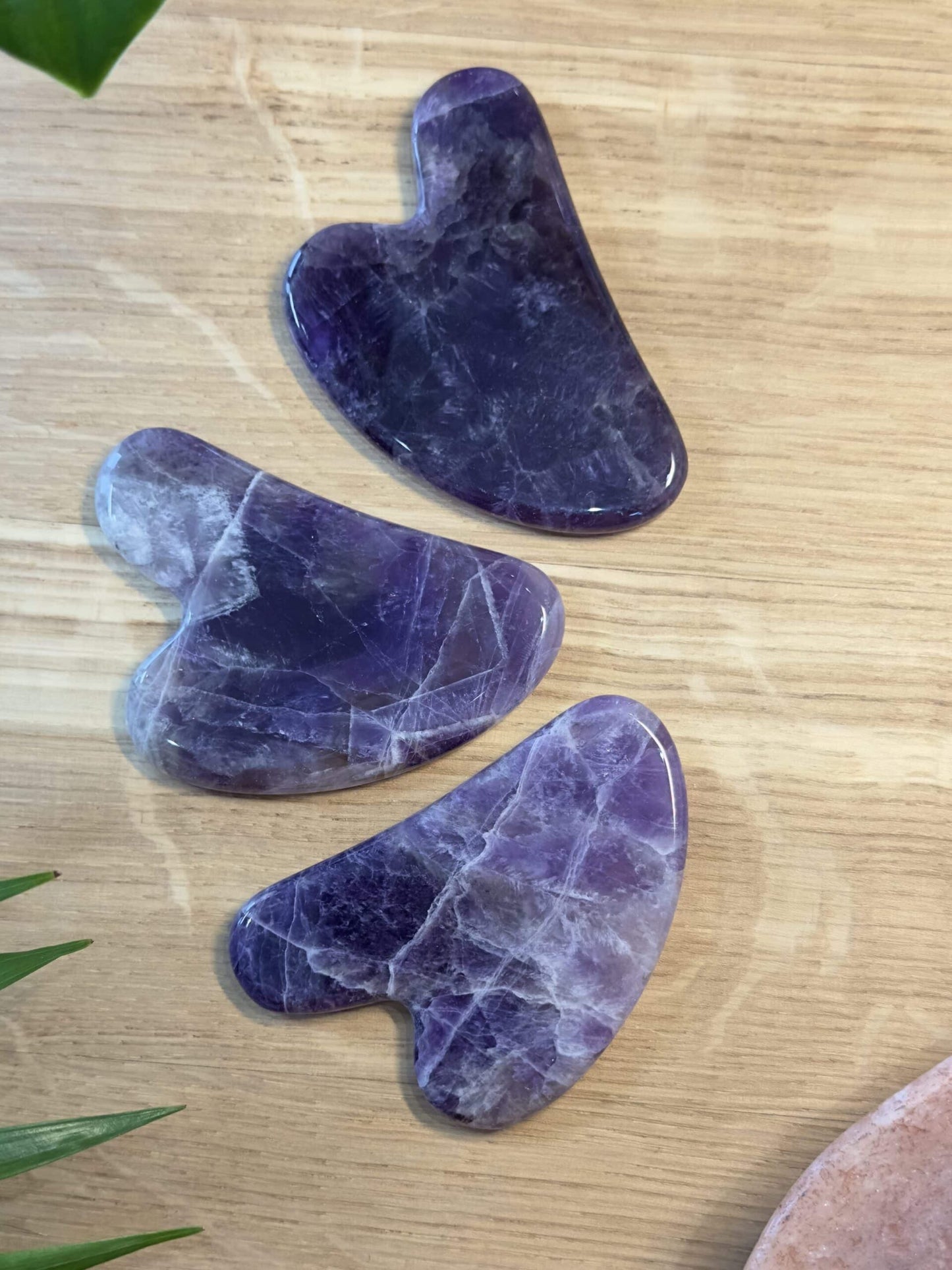Tre ametyst gua sha-sten på en træoverflade, brugt til massage og hudpleje.