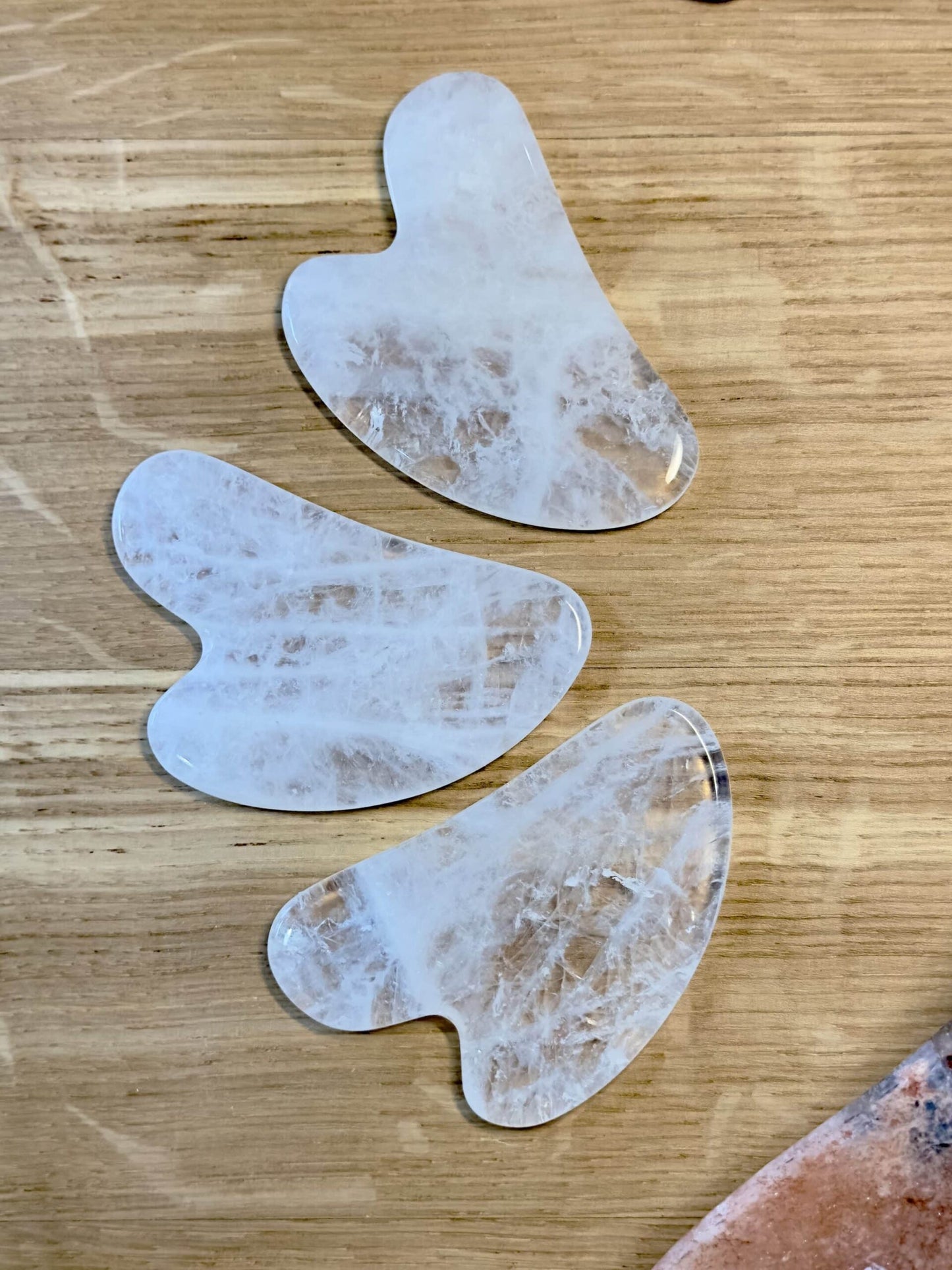 Tre stykker Bjergkrystal Gua Sha på træbord, brugt til ansigtsmassage og velvære.