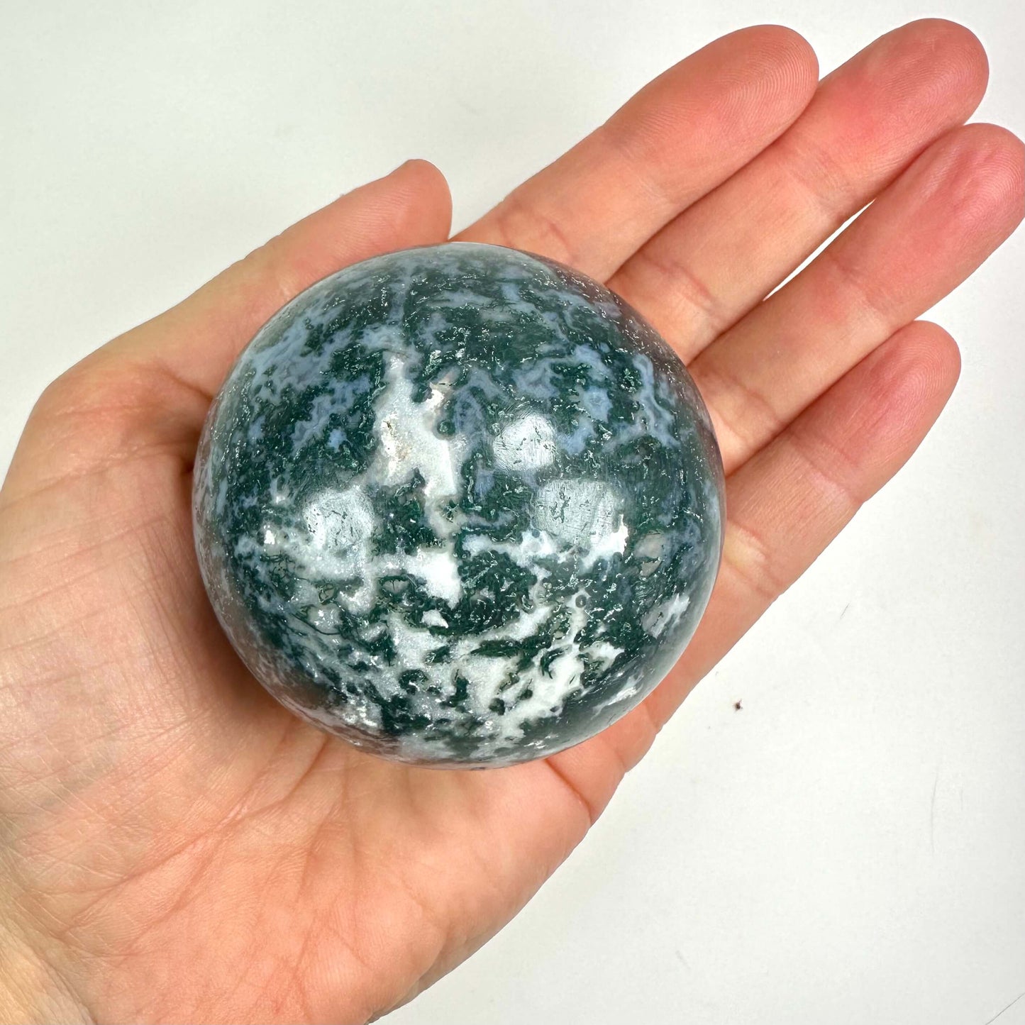 Hånd holder en kugle af mos agat med grøn og hvid marmorering.