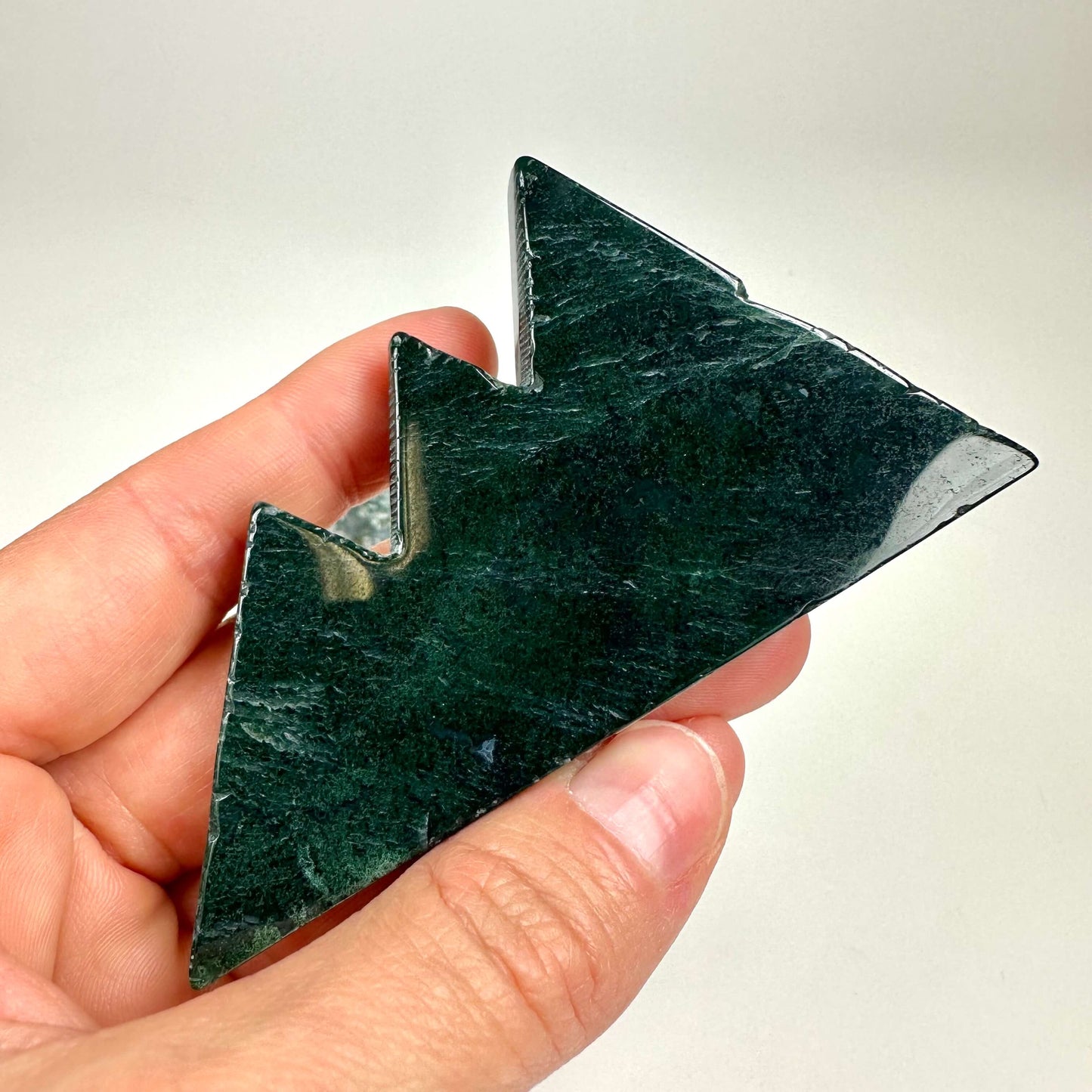 En hånd holder en mørkegrøn Mos agat formet som et bjerg.
