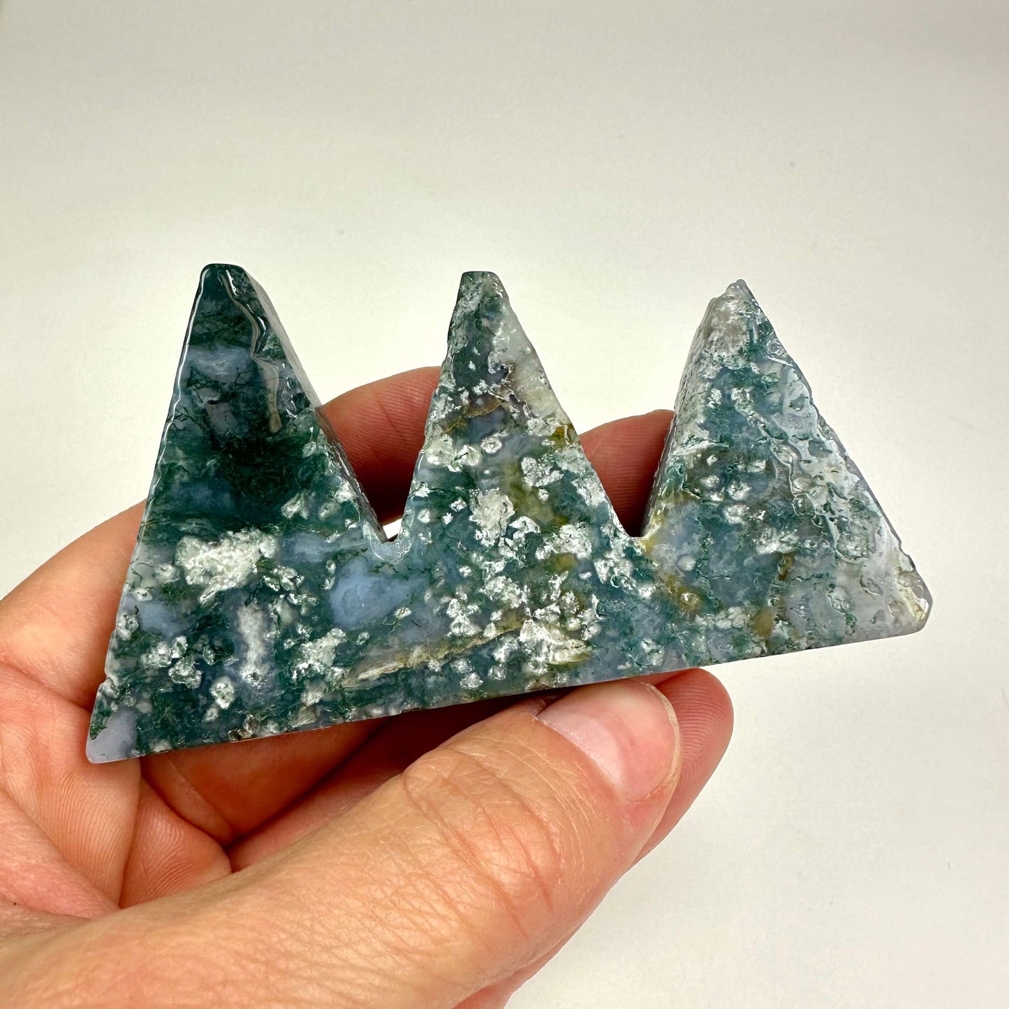 En hånd holder en trekantet sten skulptur af mos agat formet som et bjerg.