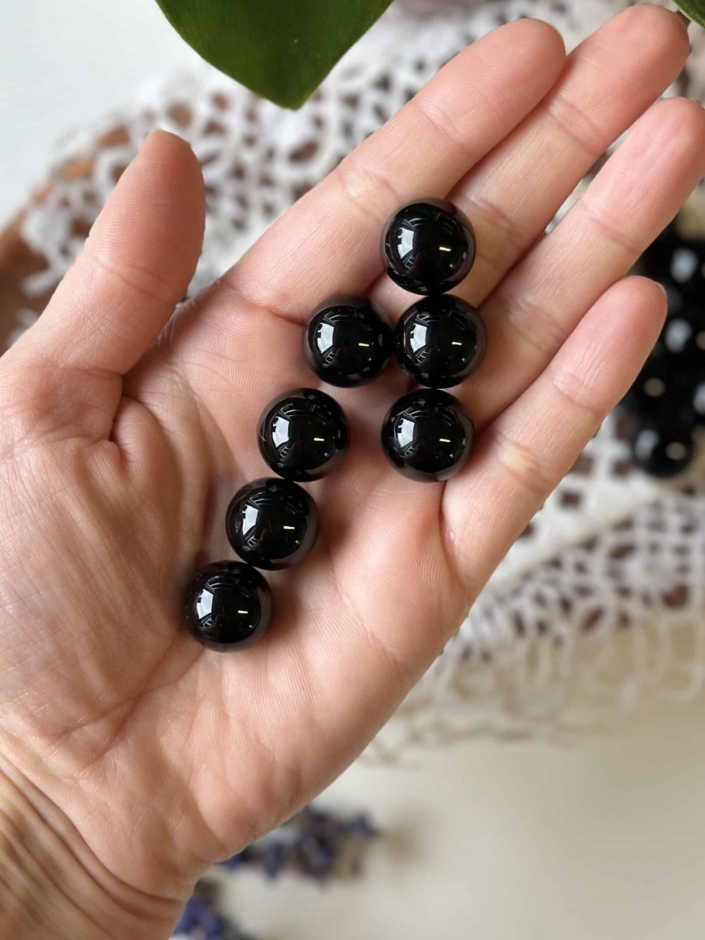En hånd holder syv Sort Agat mini kugler, som ligger på en hvid baggrund.