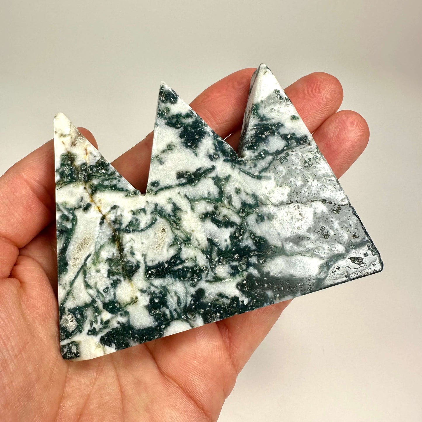 Hånd holder en dekorativ genstand af Mos agat formet som et trekantet bjerg.