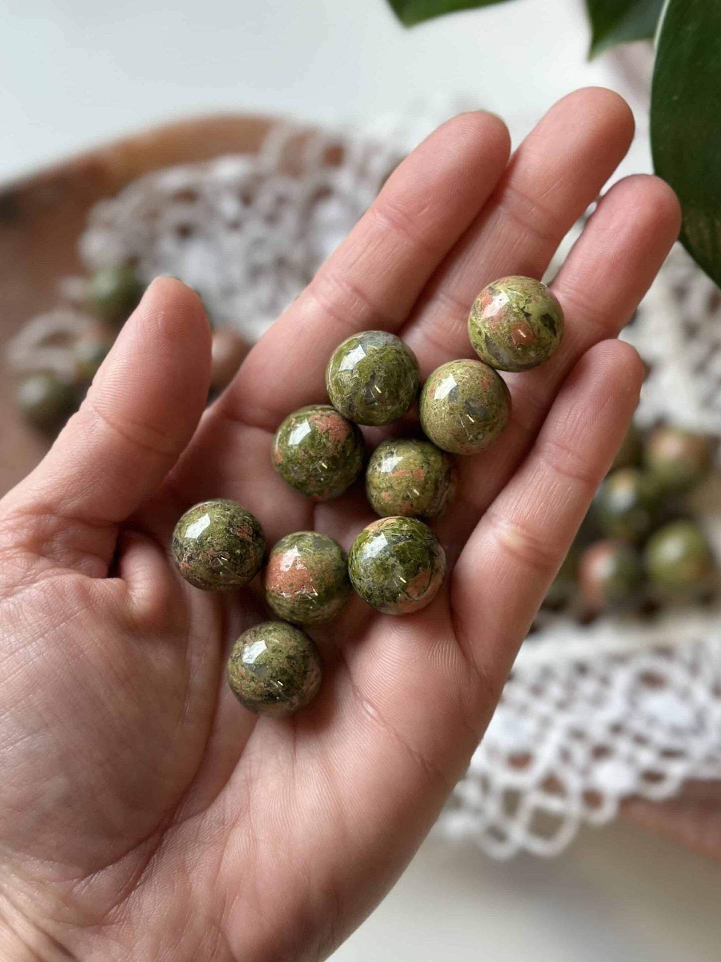 Hånd med ni Unakit mini kugler mod en baggrund af hvidt, blonderet stof.