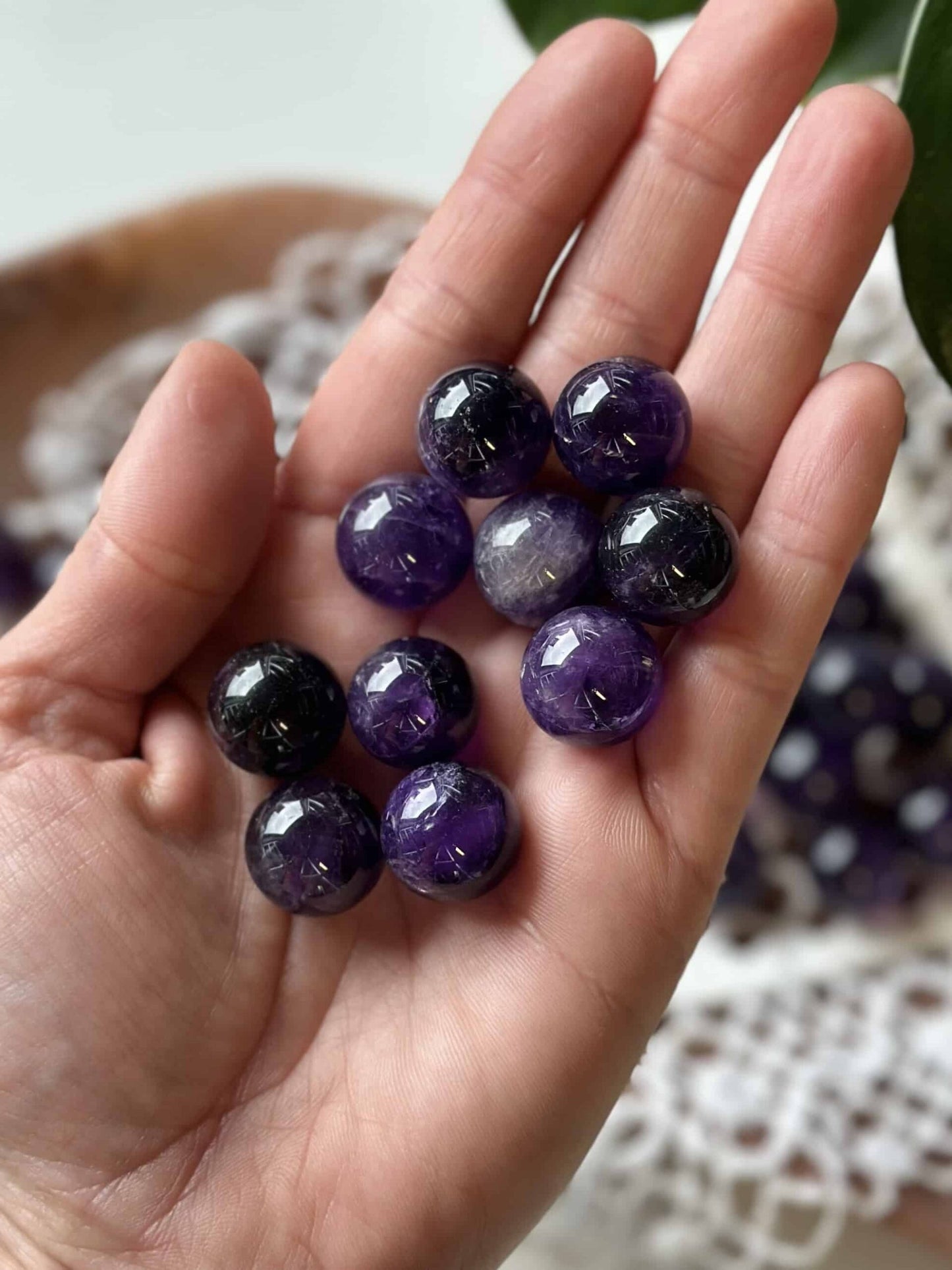 En hånd holder flere små ametyst kugler i forskellige lilla nuancer.