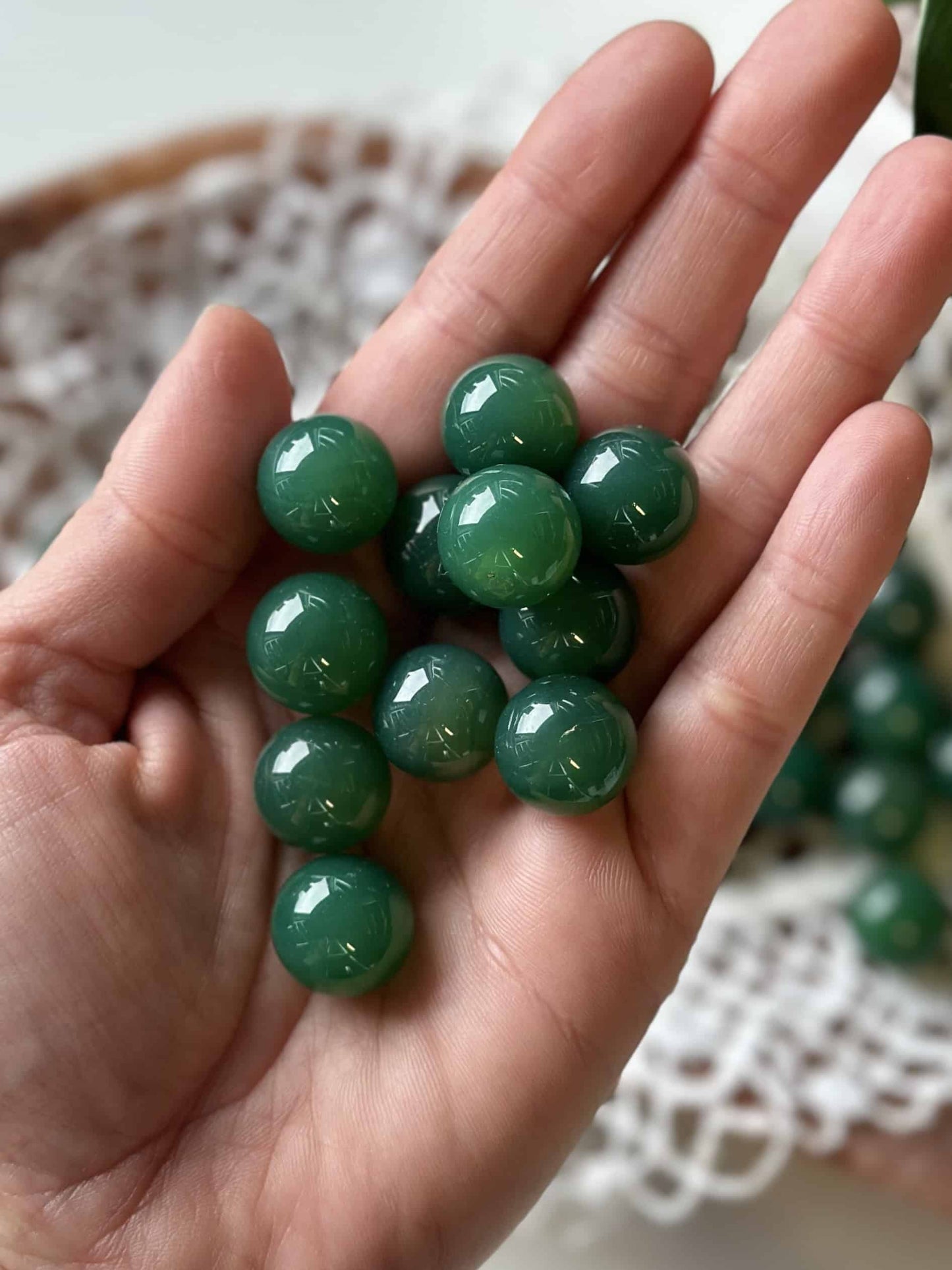 Håndfuld Grøn Agat mini kugler oven på en åben håndflade, med hvidt stof i baggrunden.