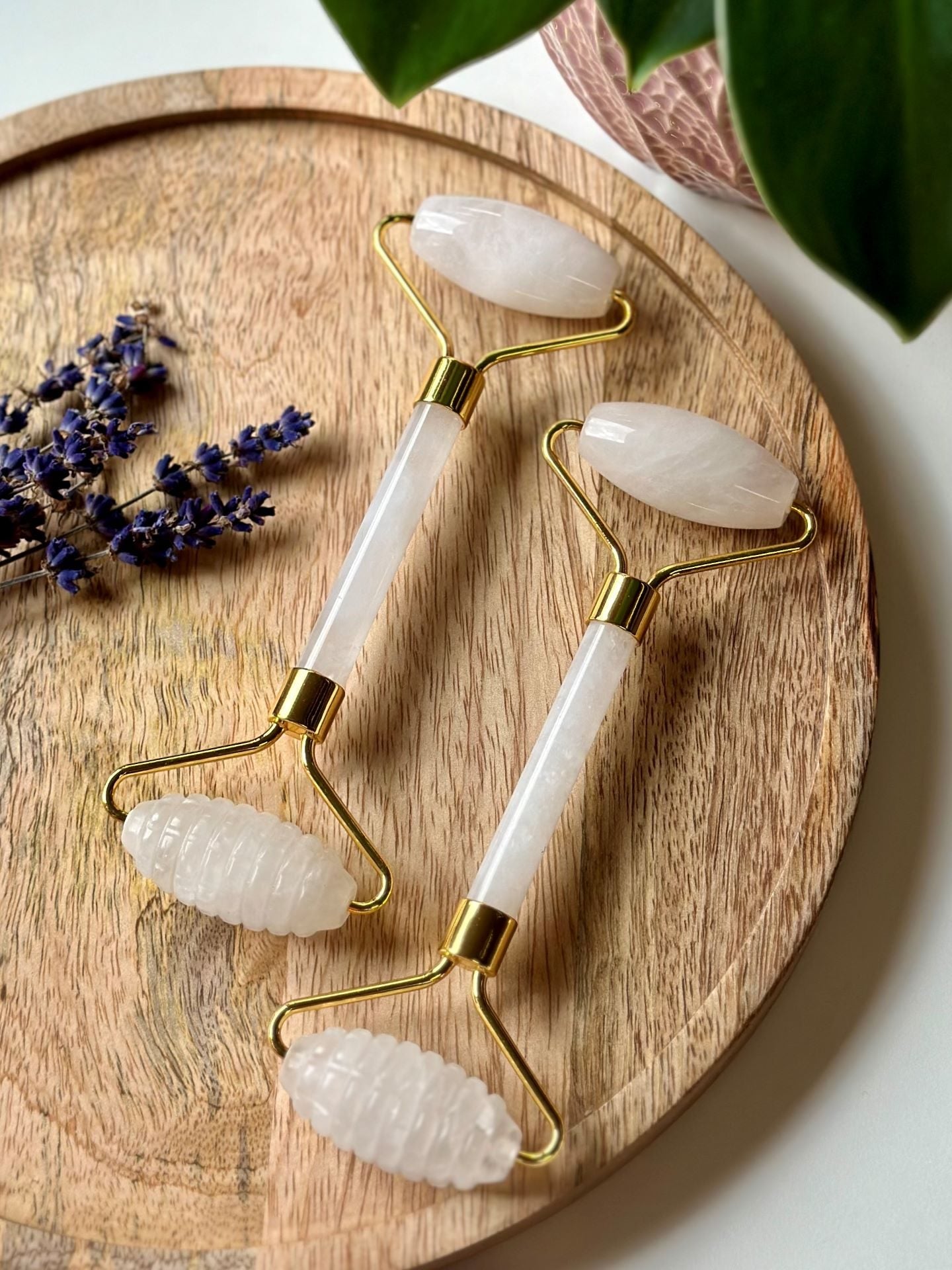 To hvid jade ansigtsruller på en træbakke med lavendel ved siden af.