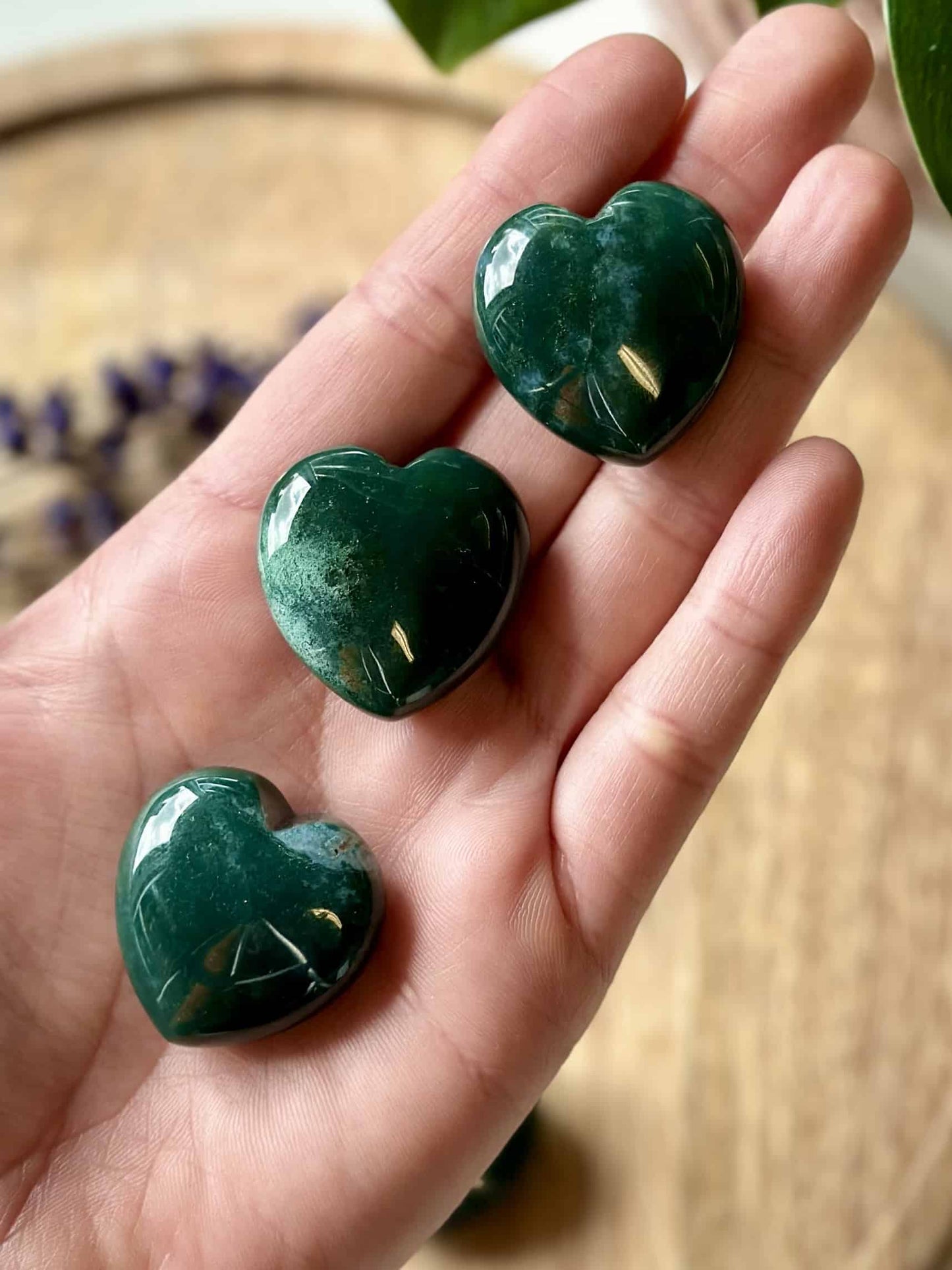 Hånd med tre hjerteformede Mos Agat sten mod en baggrund af naturmaterialer.