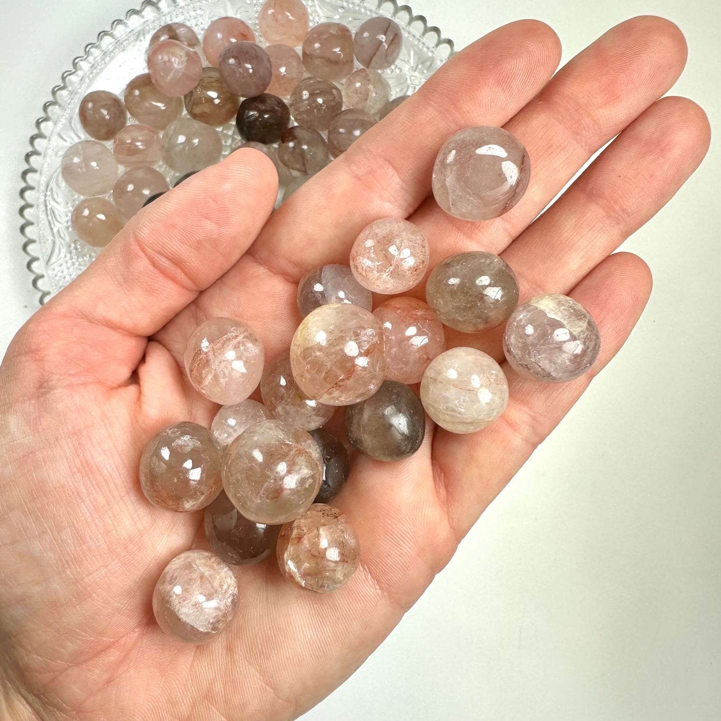 Hæmatoid krystalkugler i en hånd over en skål med flere kugler i forskellige nuancer.