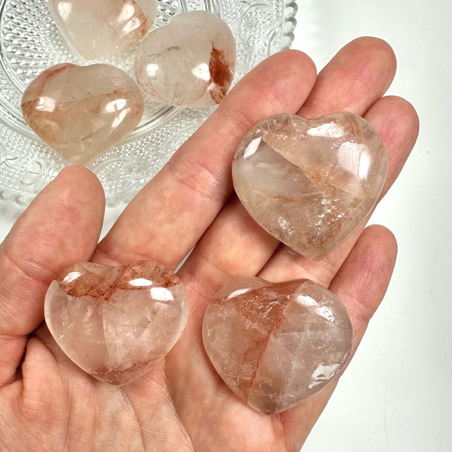 Hånd holder tre hæmatoid hjerter, med flere i en skål i baggrunden.