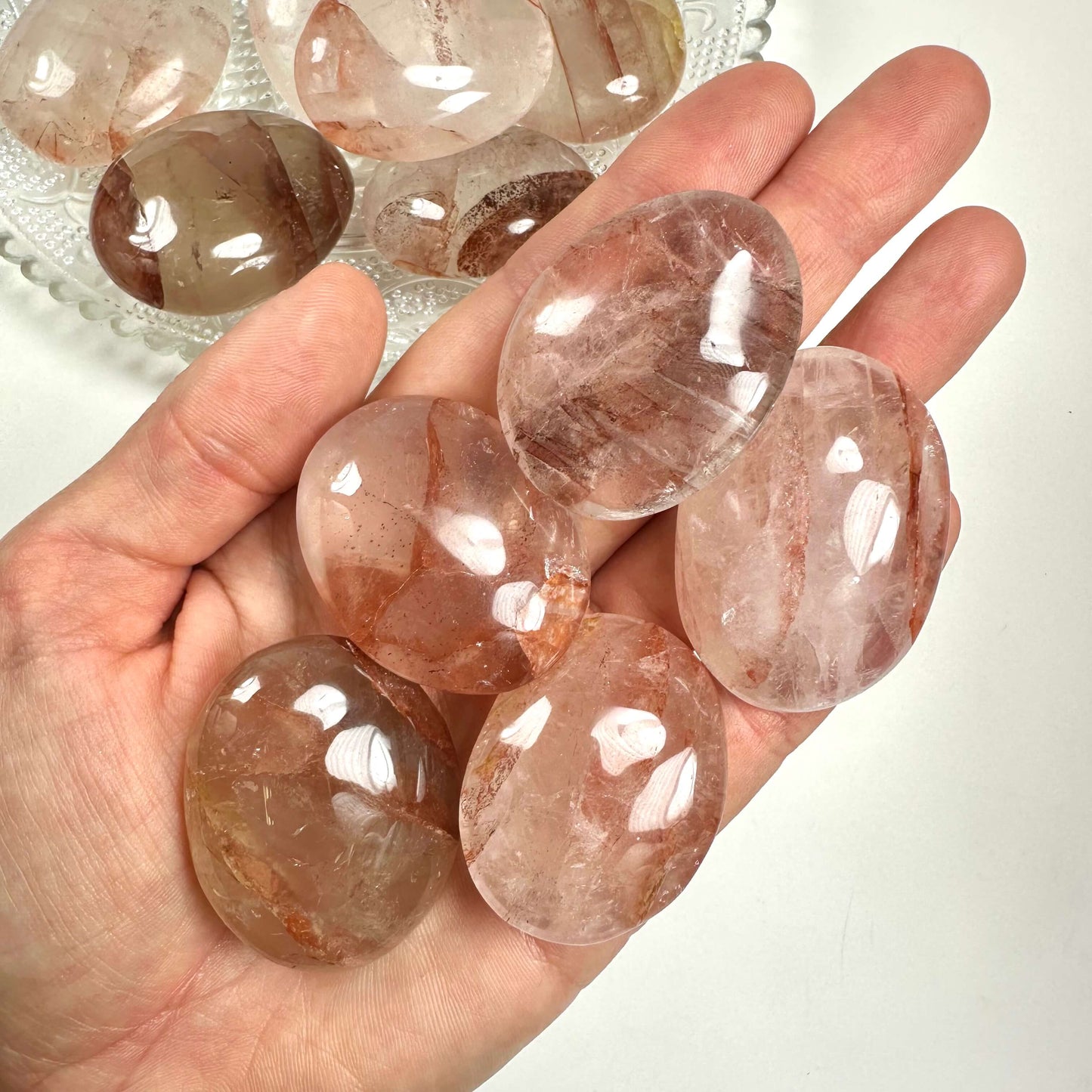 Hånd holder flere polerede, hæmatoid flad sten i forskellige nuancer af rød og pink.