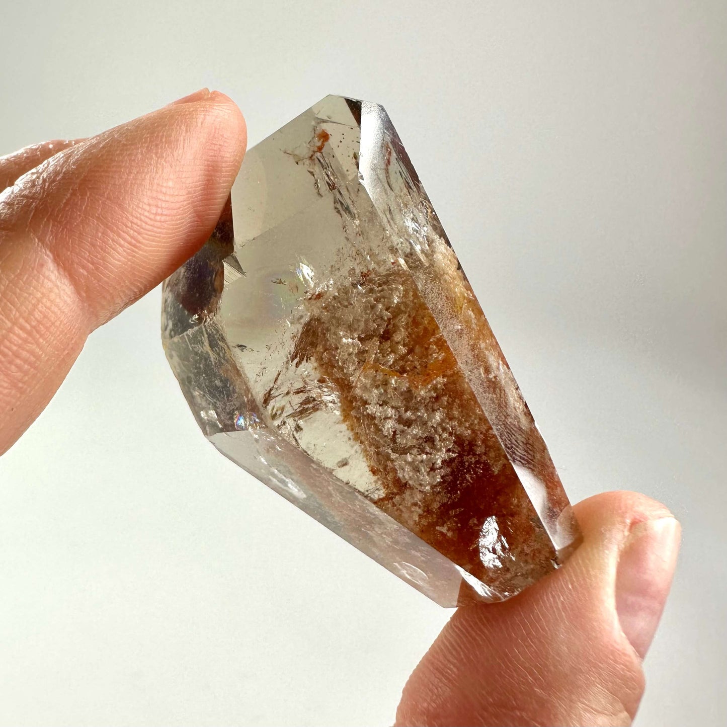 Fantomkvarts fri form holdes mellem fingerspidserne med detaljeret struktur indeni.