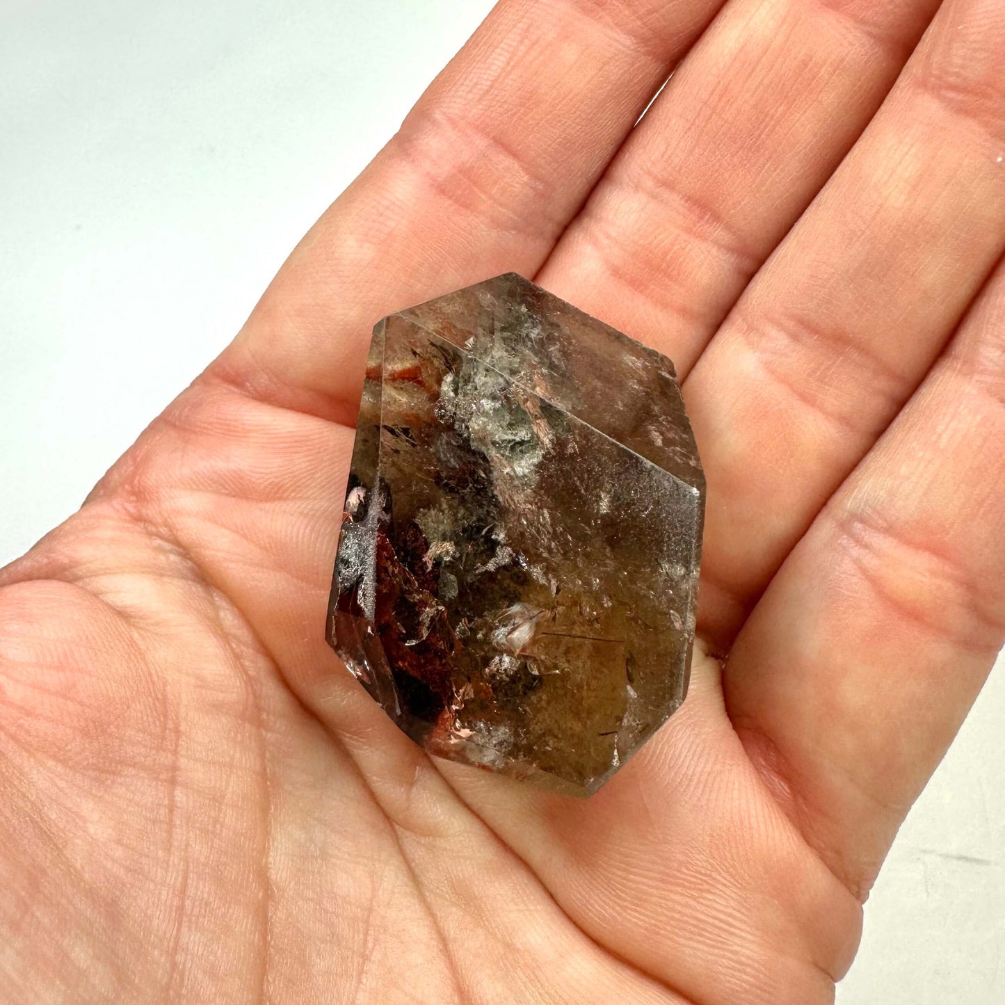 Hånd, der holder en fri form af Fantomkvarts med naturlige indeslutninger og brune nuancer.