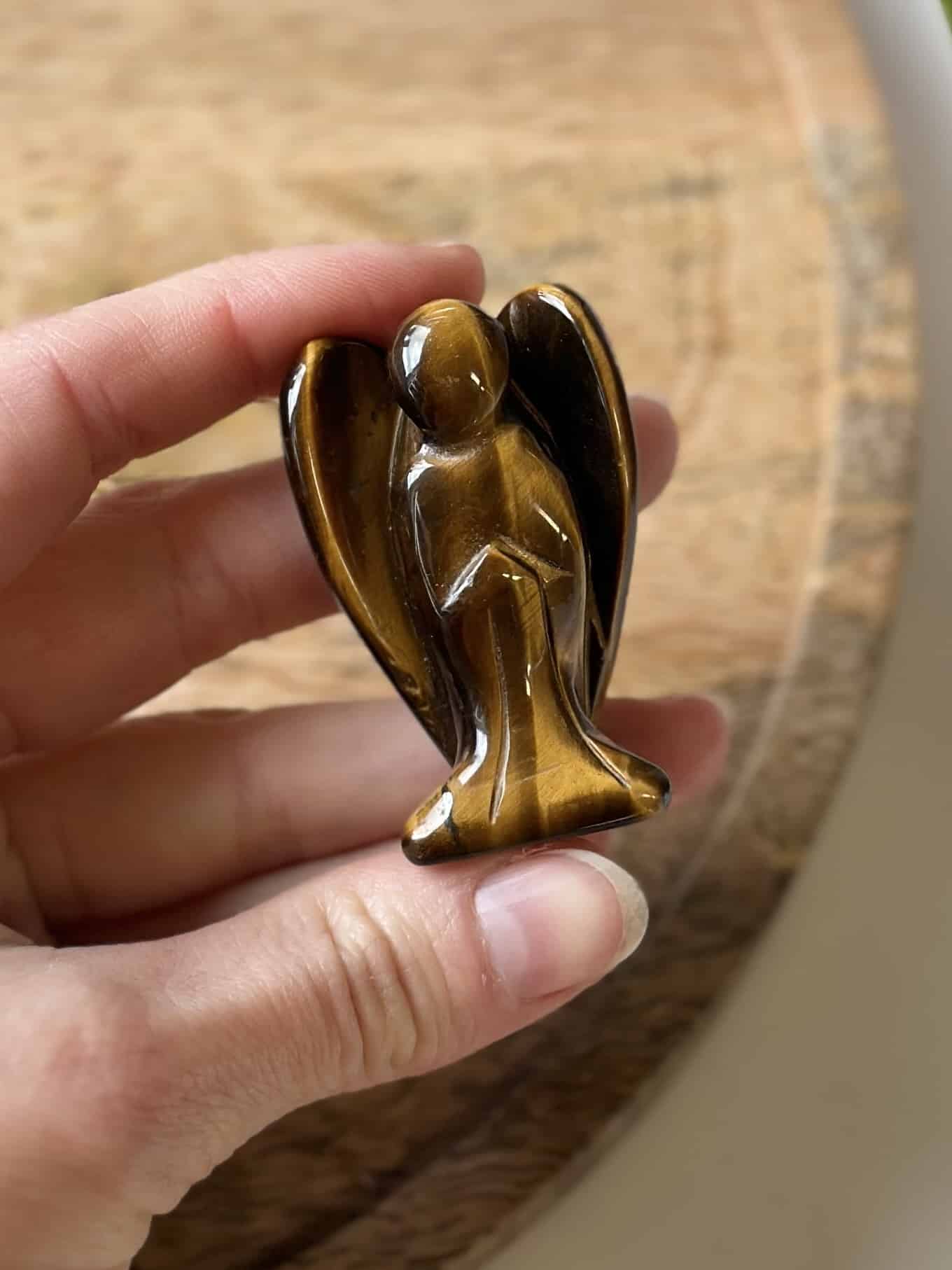 Hånd holder en skulptur af en engel lavet af tigerøje-sten.