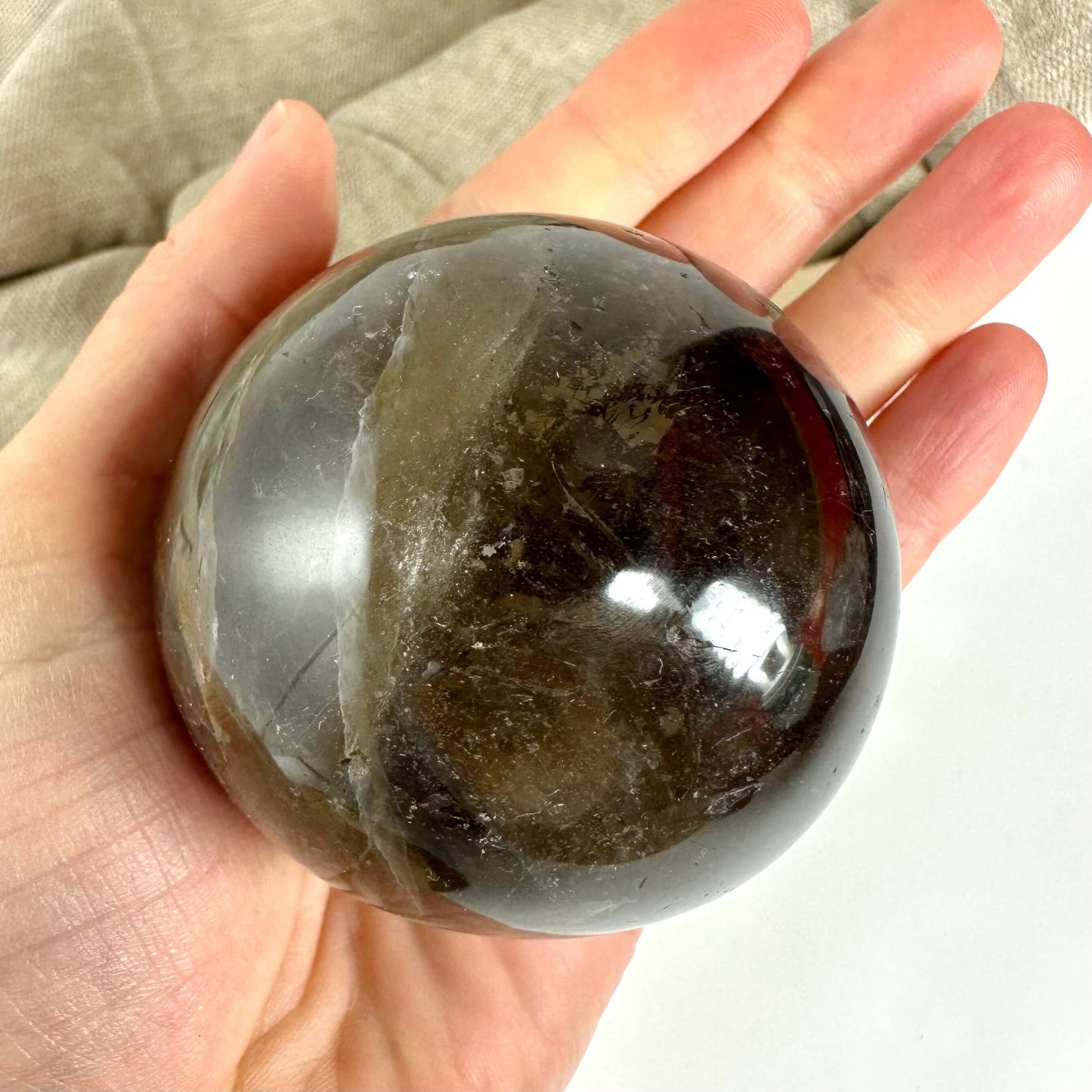 Hånd holder en skinnende, rund Røgkvarts kugle mod en lys baggrund.