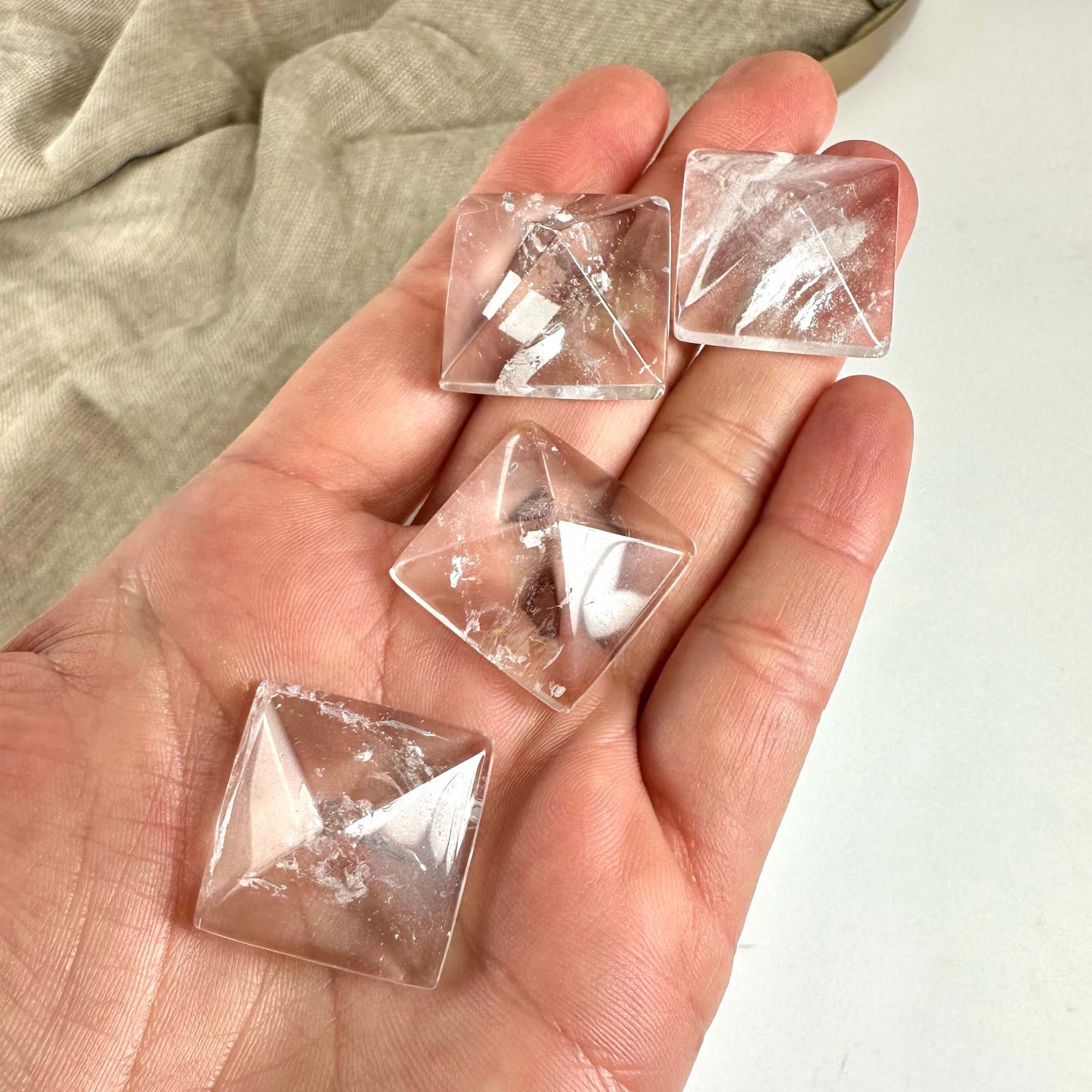 Hånd holder fire små bjergkrystal pyramider på en beige klud baggrund.