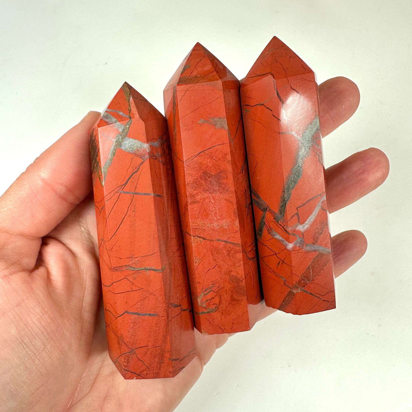 Tre røde jaspis tårne holdes i en hånd, med synlige naturlige mønstre og årer.