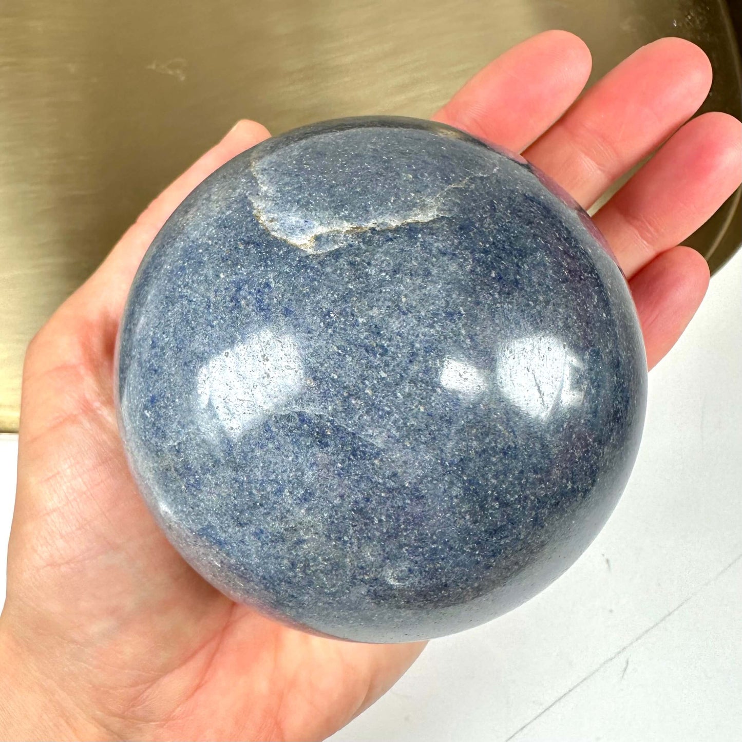 Person holder en rund Dumortierit-kugle i hånden, med en blålig struktur og en lille revne.