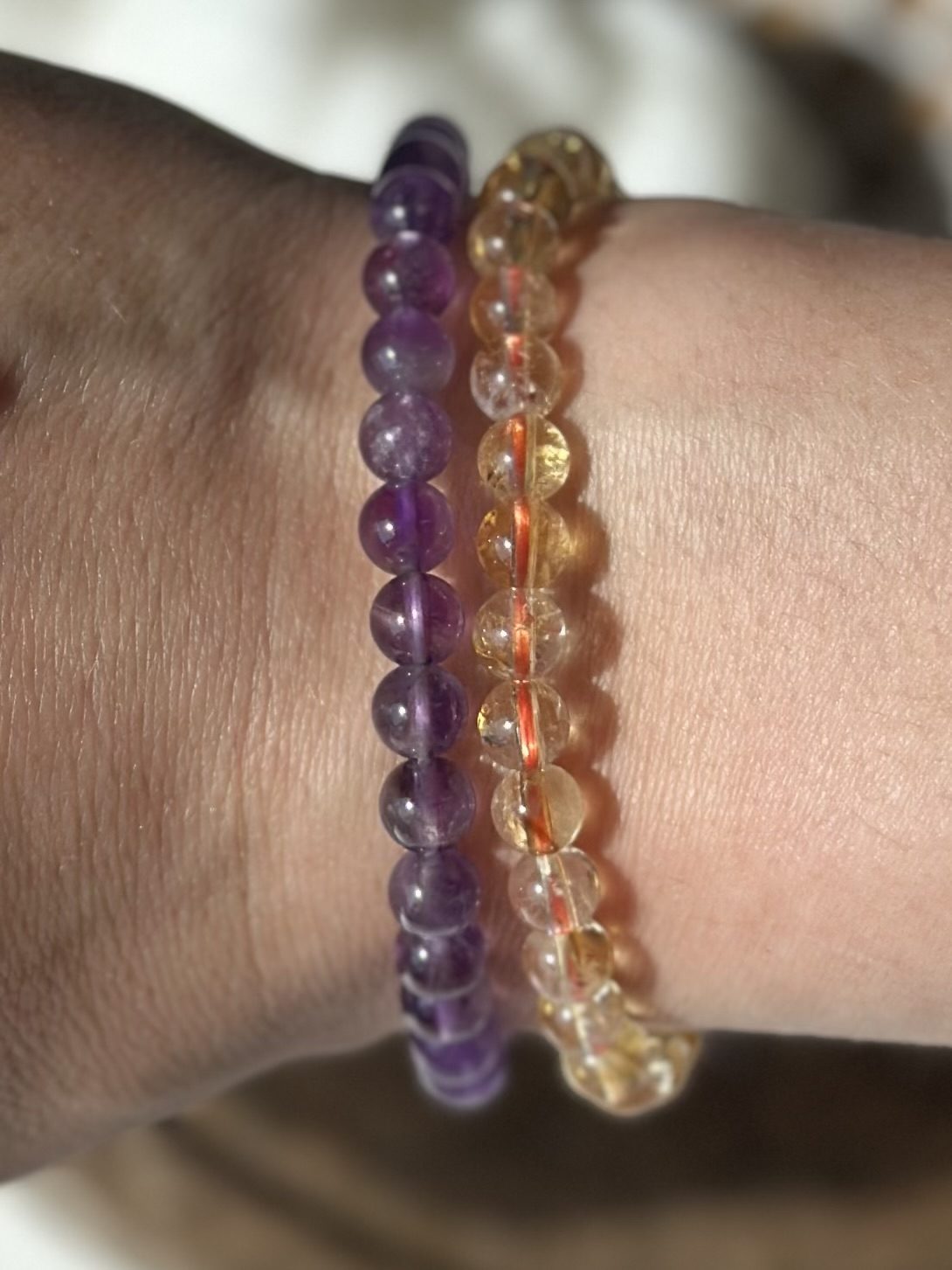 To farverige armbånd lavet af perler; det ene lilla og det andet gul-orange, på en håndled. Eksamens sæt.