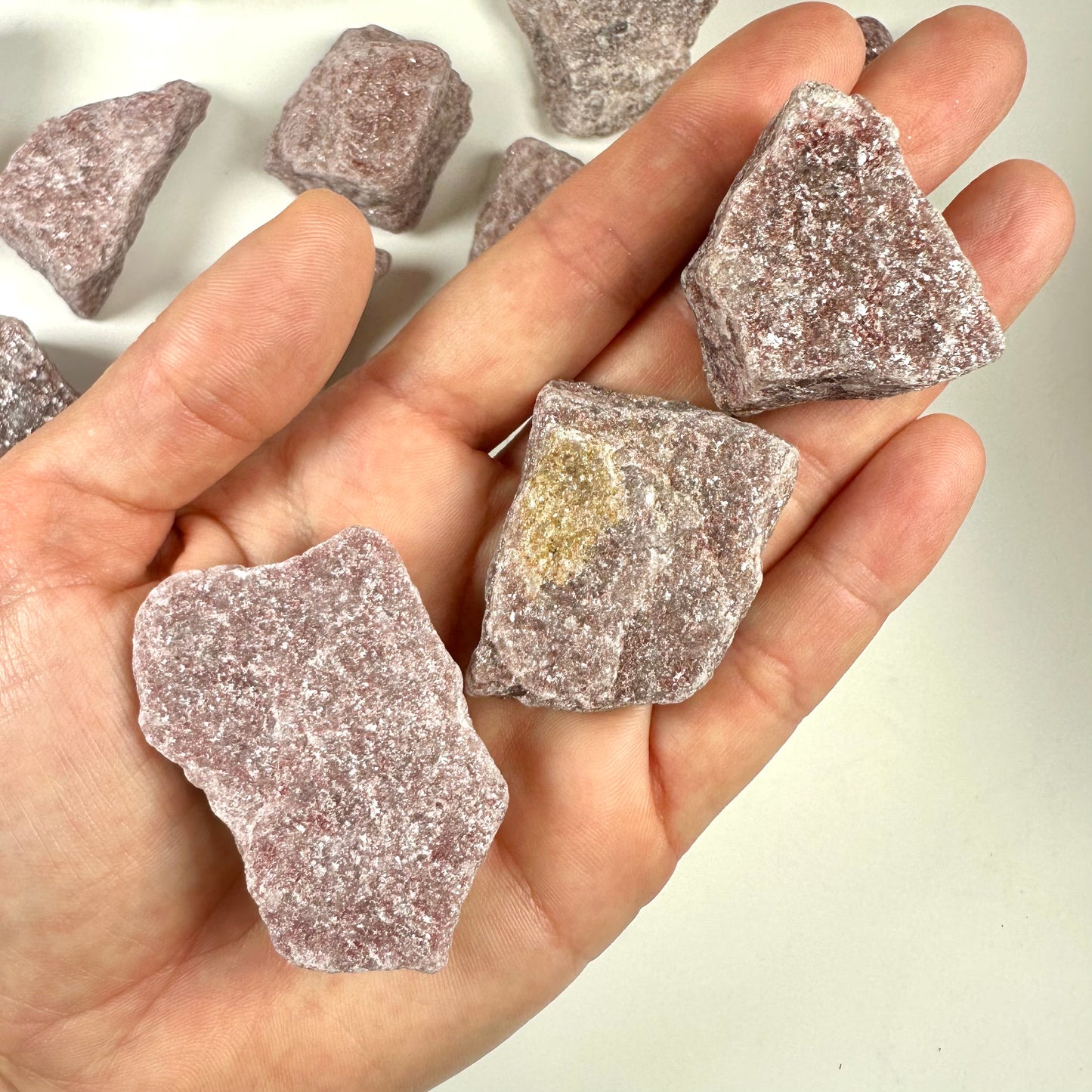 Hånden holder flere stykker kvartsit bordeaux mod en lys baggrund.