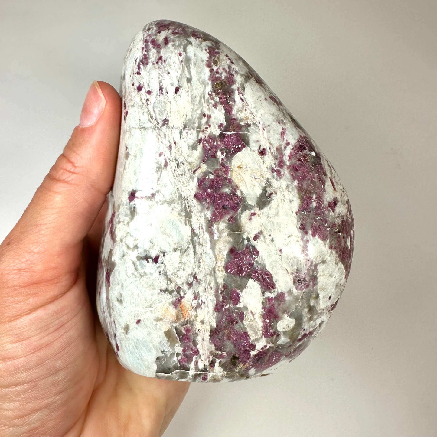 Hånd holder en Rubellit kvarts free form med hvide og lilla nuancer mod en lys baggrund.