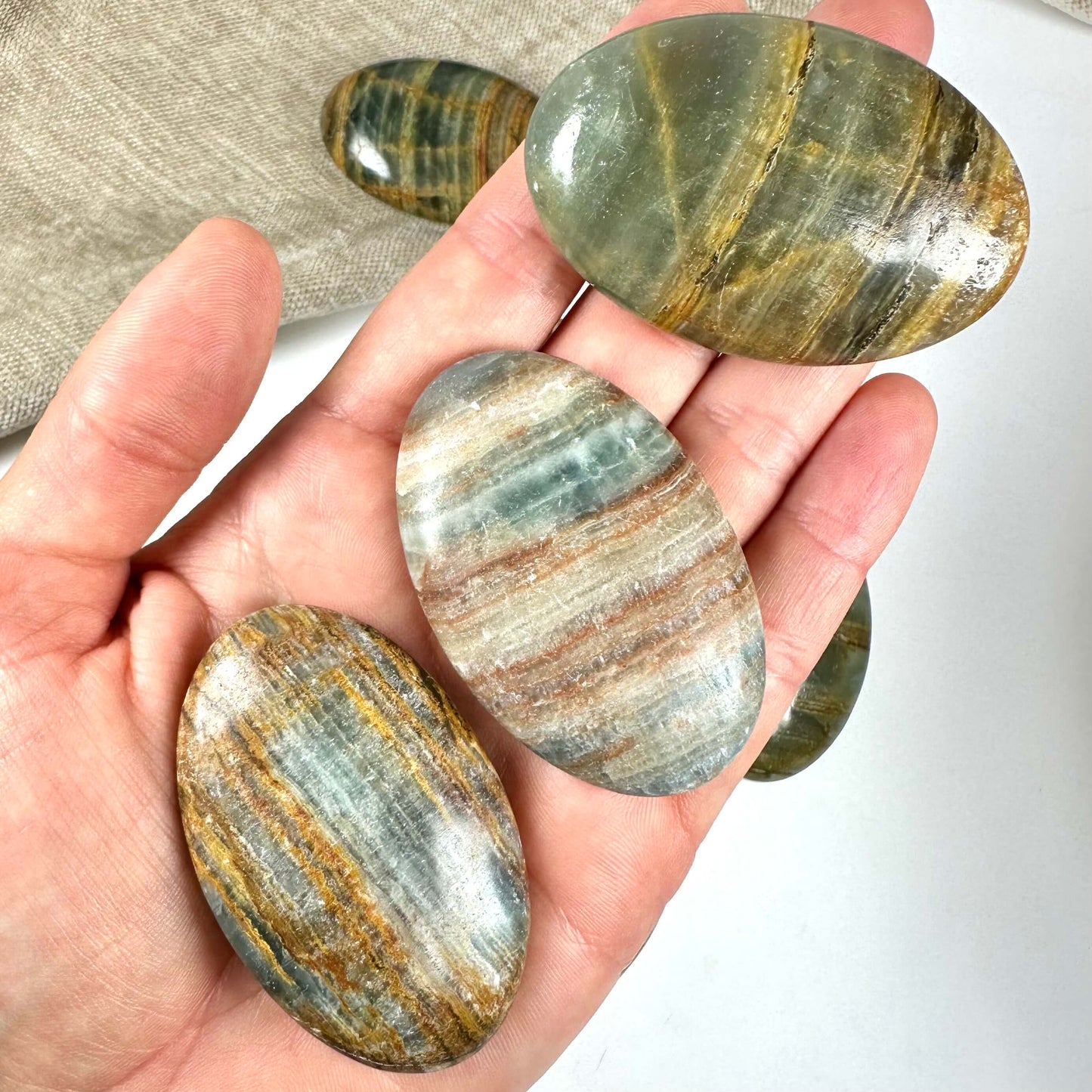 Hånd holder flere ovale blå onyx flad sten med stribede farvemønstre.
