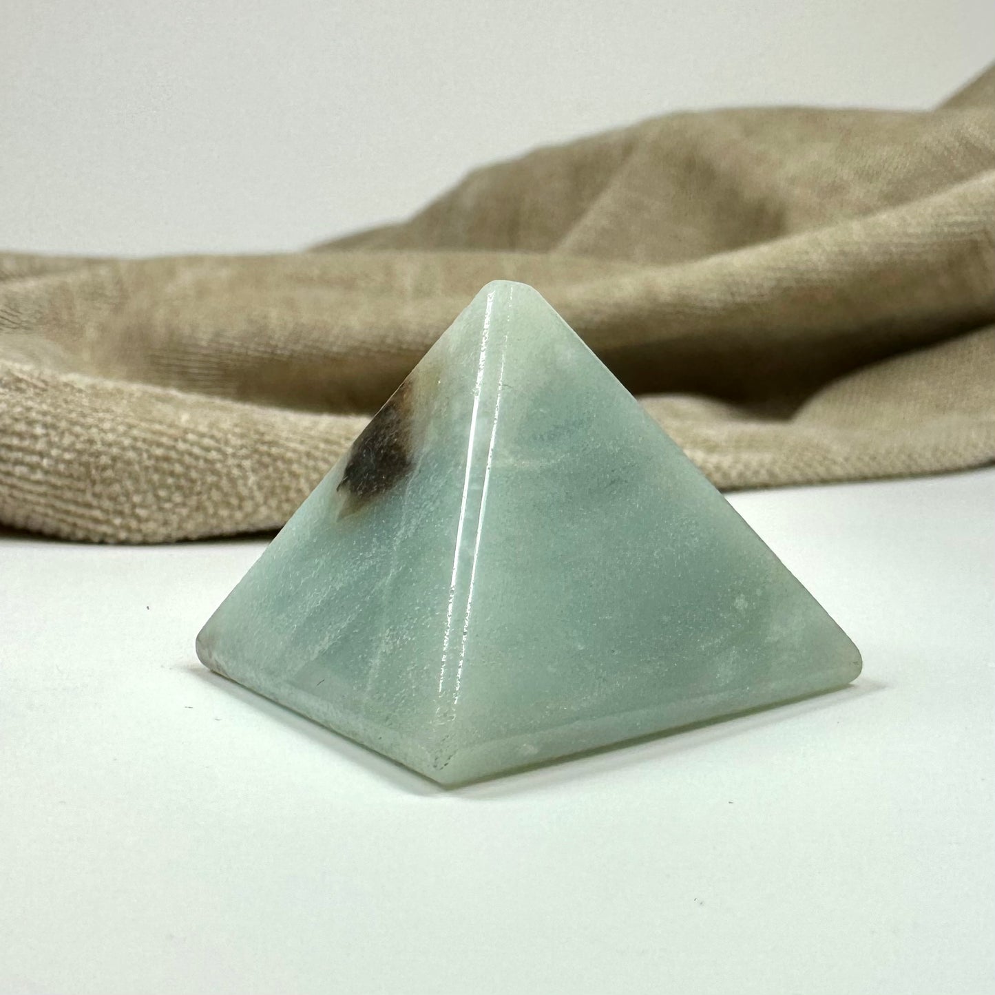 Amazonitpyramide foran beige stofbaggrund.