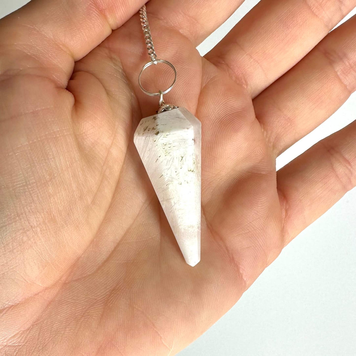 En hånd holder et Scolesit pendul med en kæde og ring, set tæt på.