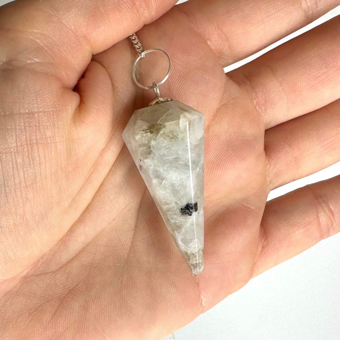 Hånd, der holder et regnbue månesten pendul med en kæde vedhængende.