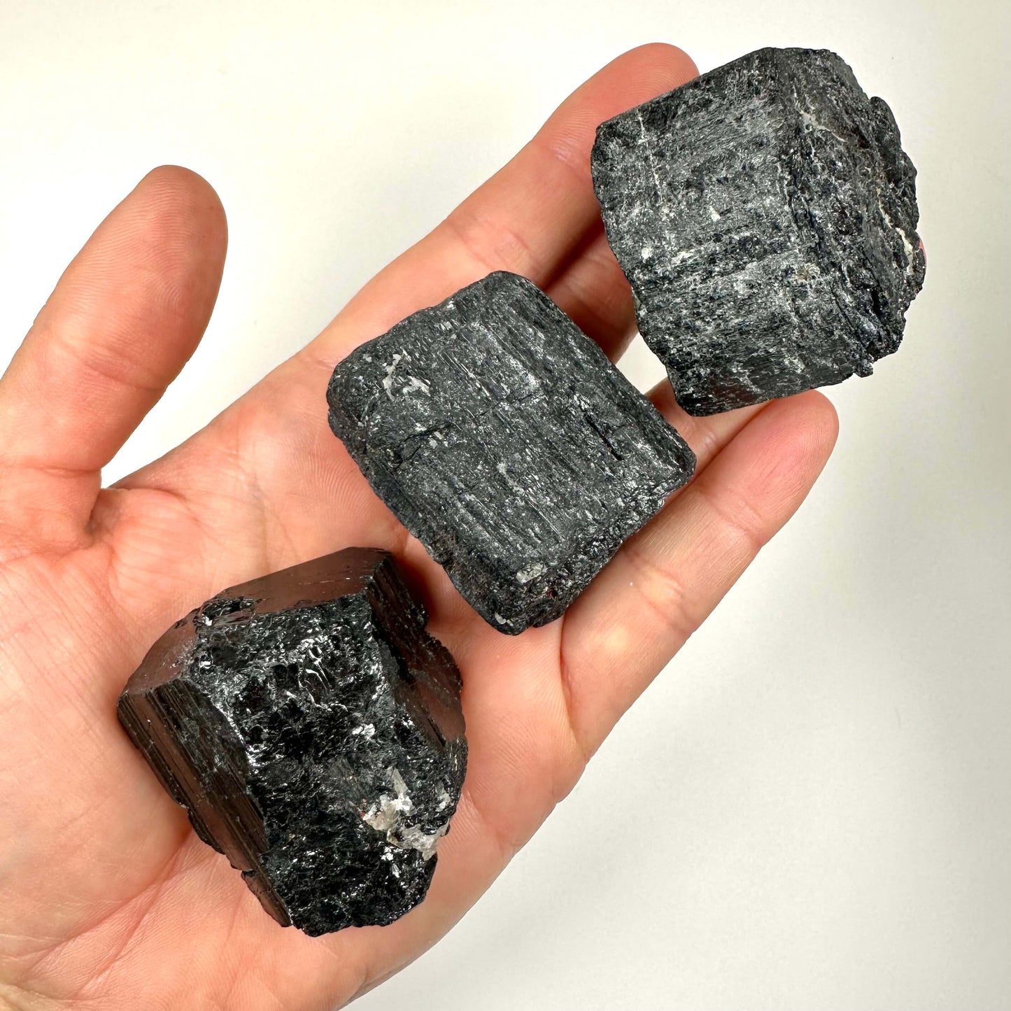 Hånd viser tre stykker sort turmalin rå sten, tæt på.
