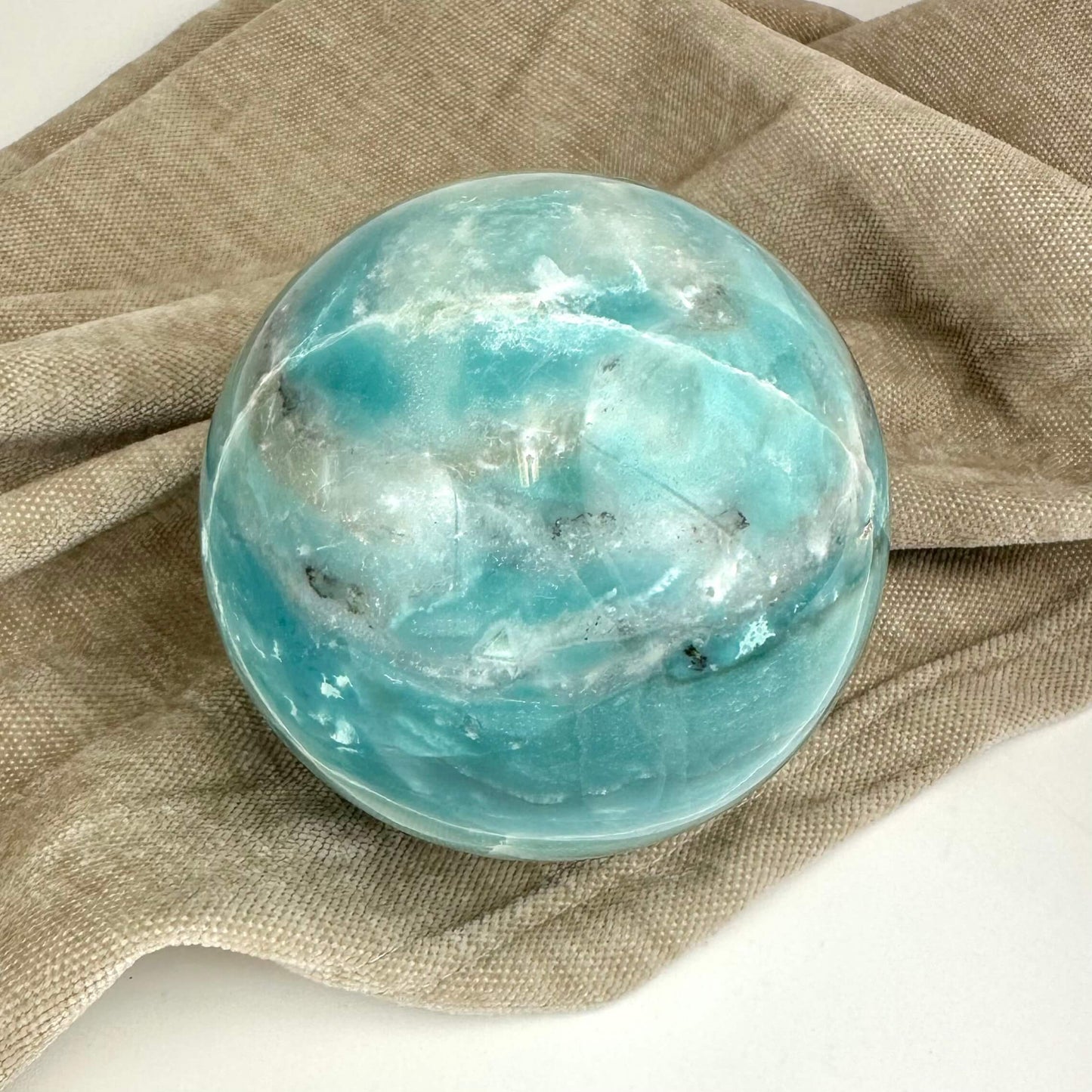 Amazonit kugle i turkis og hvid på en beige klud.