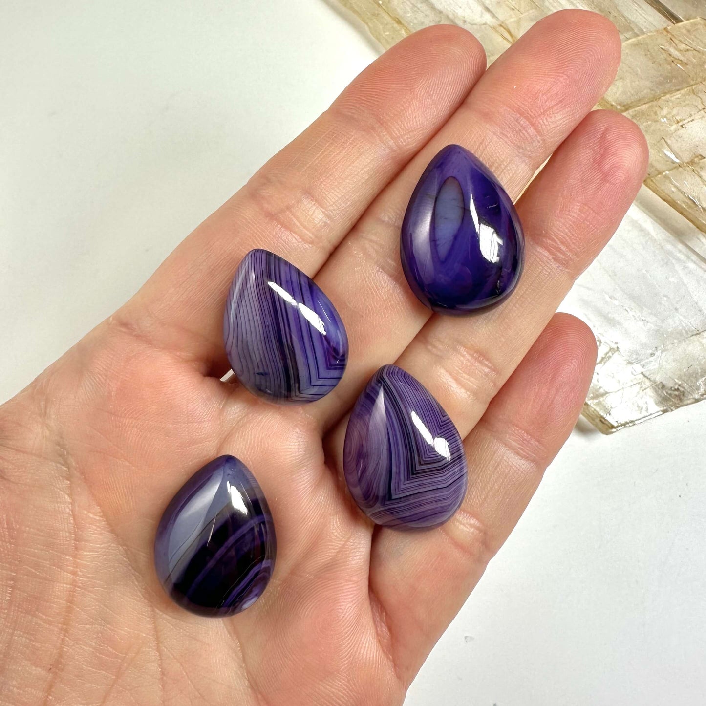 Hånd holder fire lilla agat dråbeformede sten med stribede mønstre.