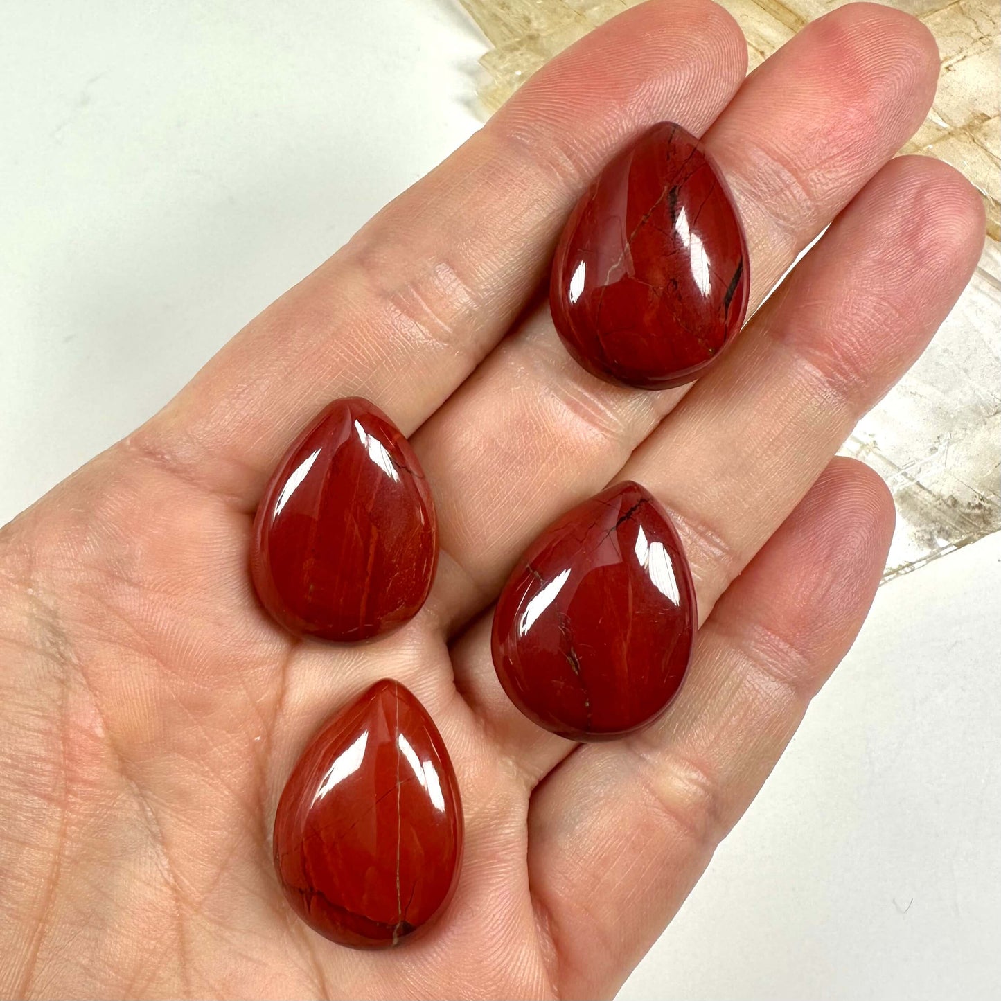 Fire Rød jaspis dråbe-sten ligger i en hånd på hvid baggrund.
