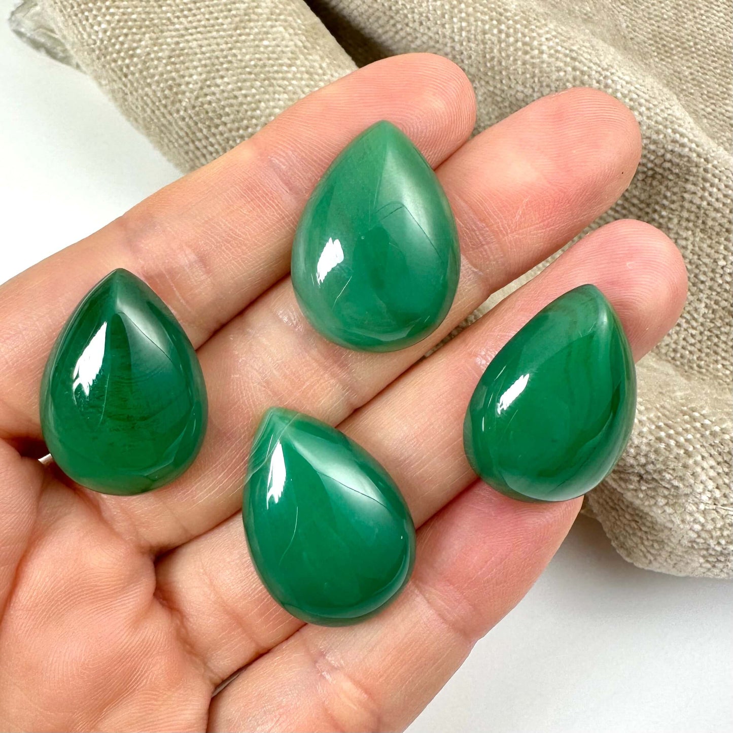 Fire grøn agat dråbe-sten ligger på en hånd med beige stof i baggrunden.