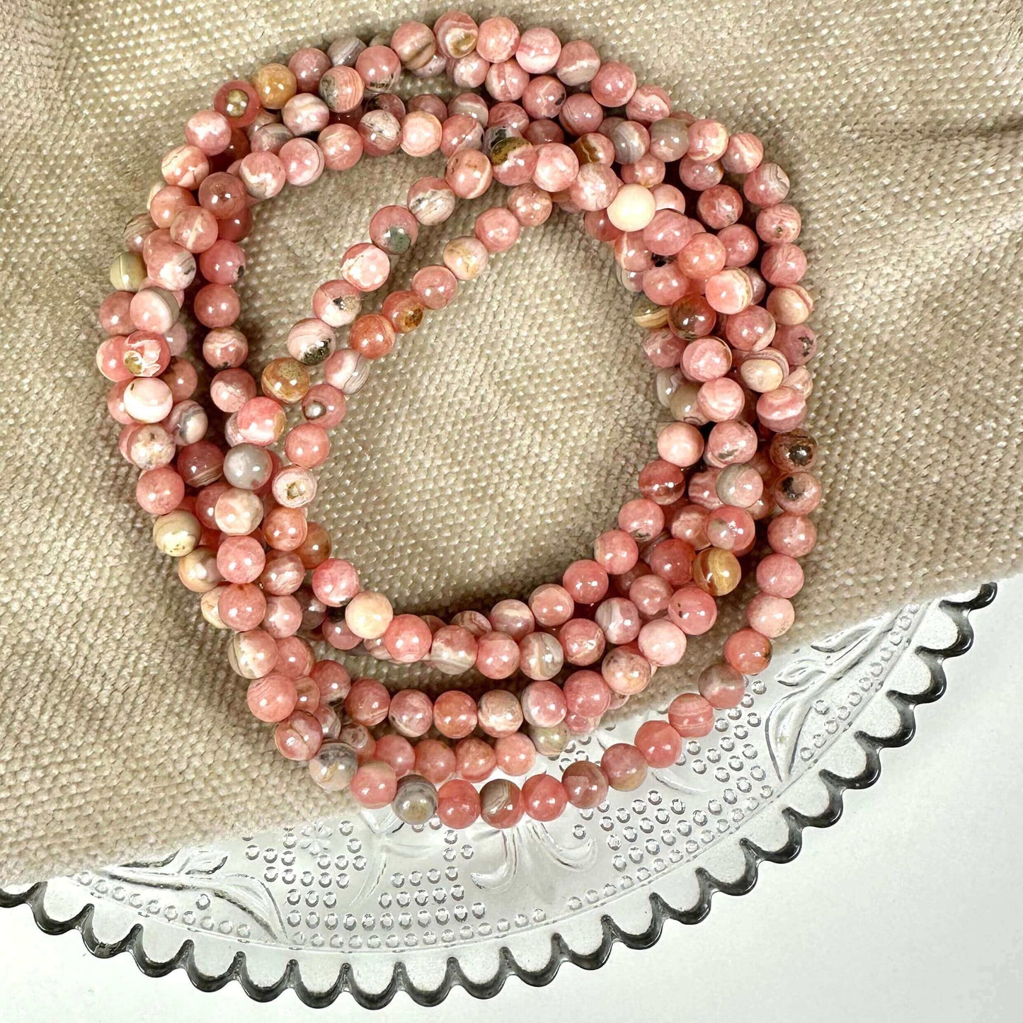 Lyserøde perlekæder arrangeret på en beige stofbaggrund og en dekoreret glasplade.