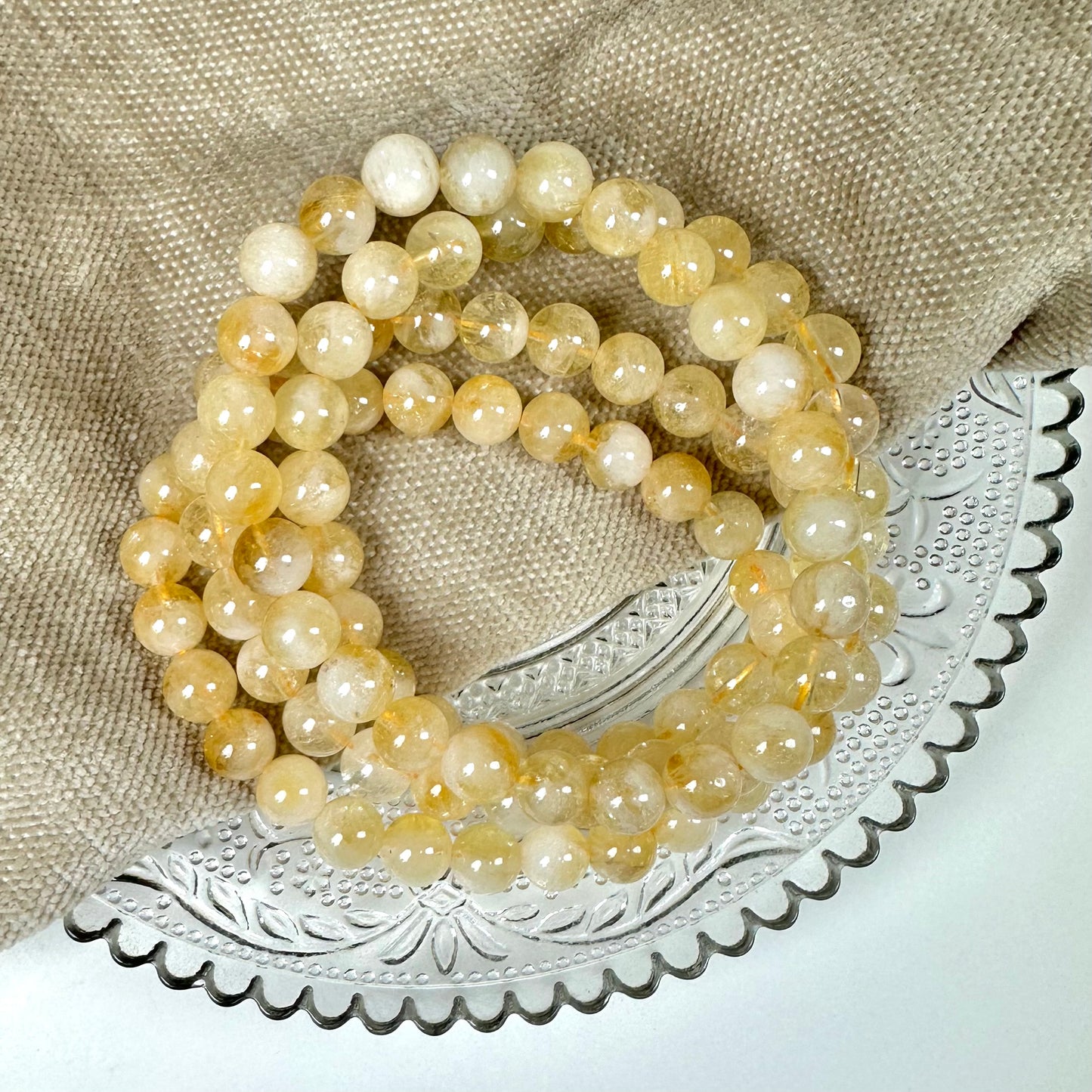 En række gule perler ligger på en beige stofpose ovenpå en dekorativ glasplade.