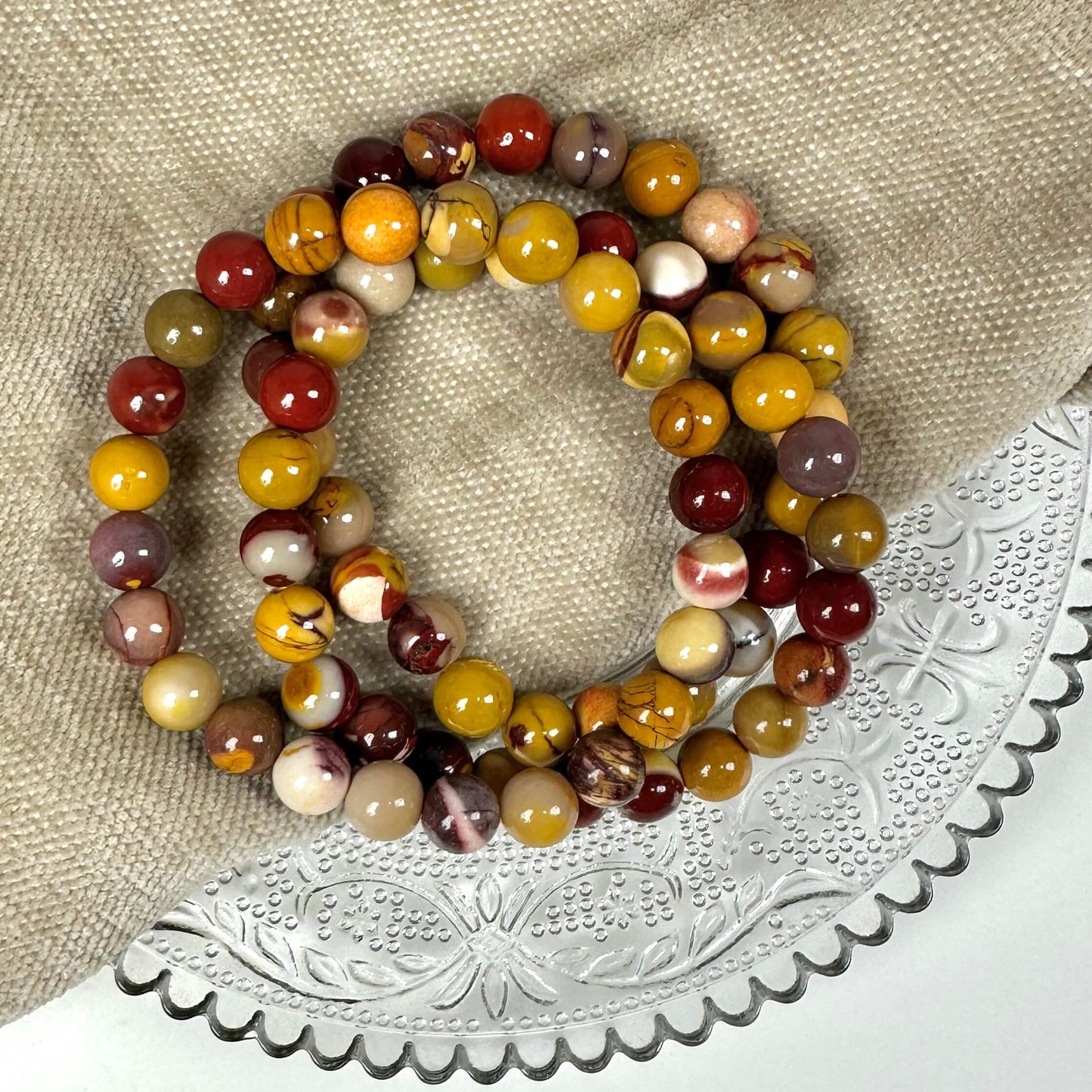 To armbånd af flerfarvet perler ligger på en neutral klud og dekoreret glasfad.