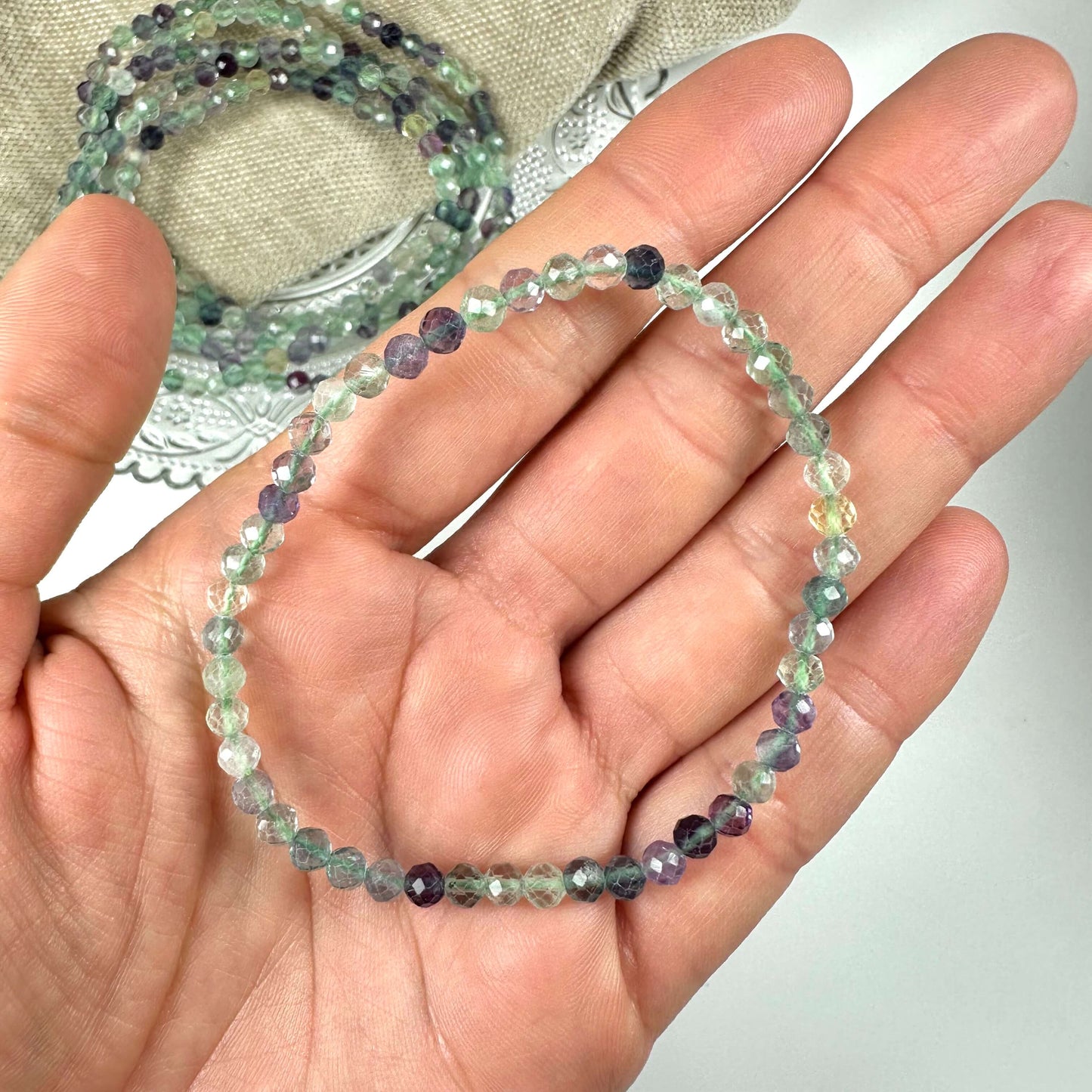 En hånd holder et Fluorit armbånd med multifarvede perler på en lys baggrund.