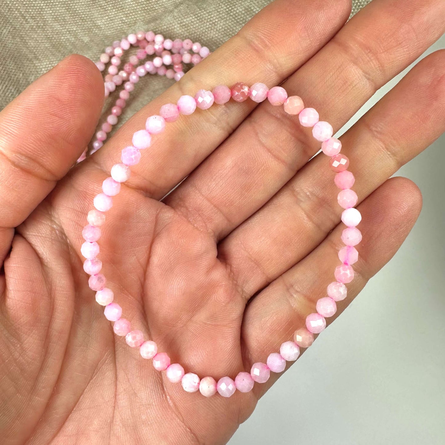 En hånd holder et pink opal armbånd med 4mm facetperler.