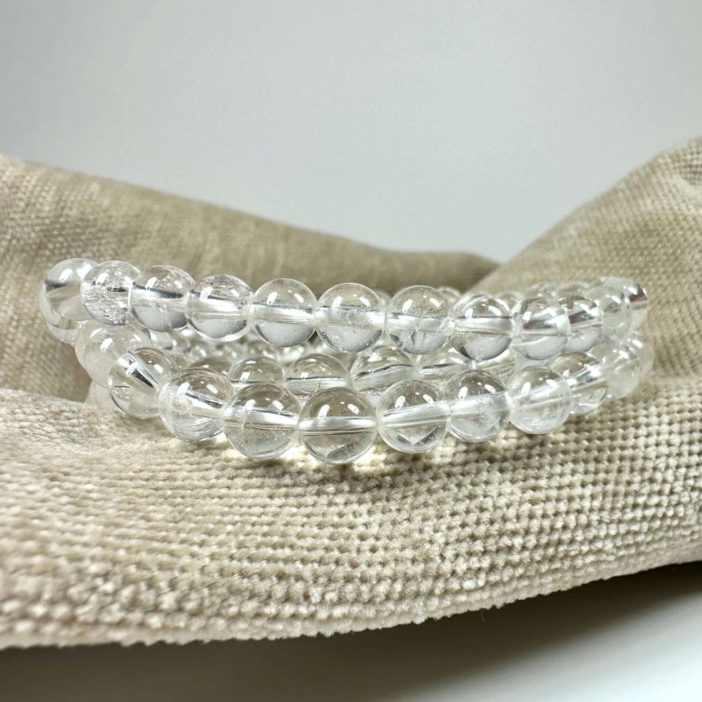 Bjergkrystal armbånd på beige stofbaggrund med klare, runde perler i to rækker.