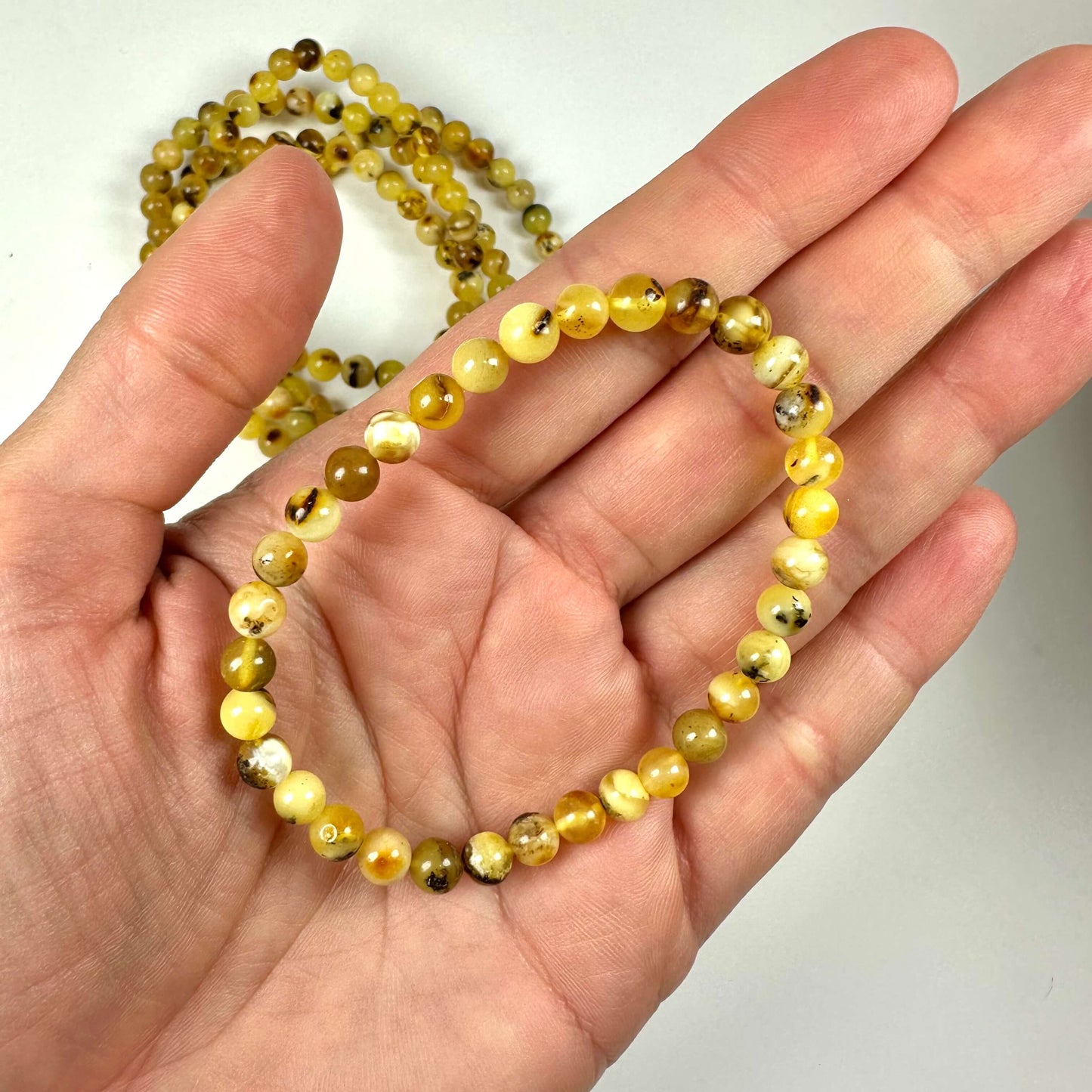 En hånd, der holder et gult rav armbånd på 5 mm med runde perler.