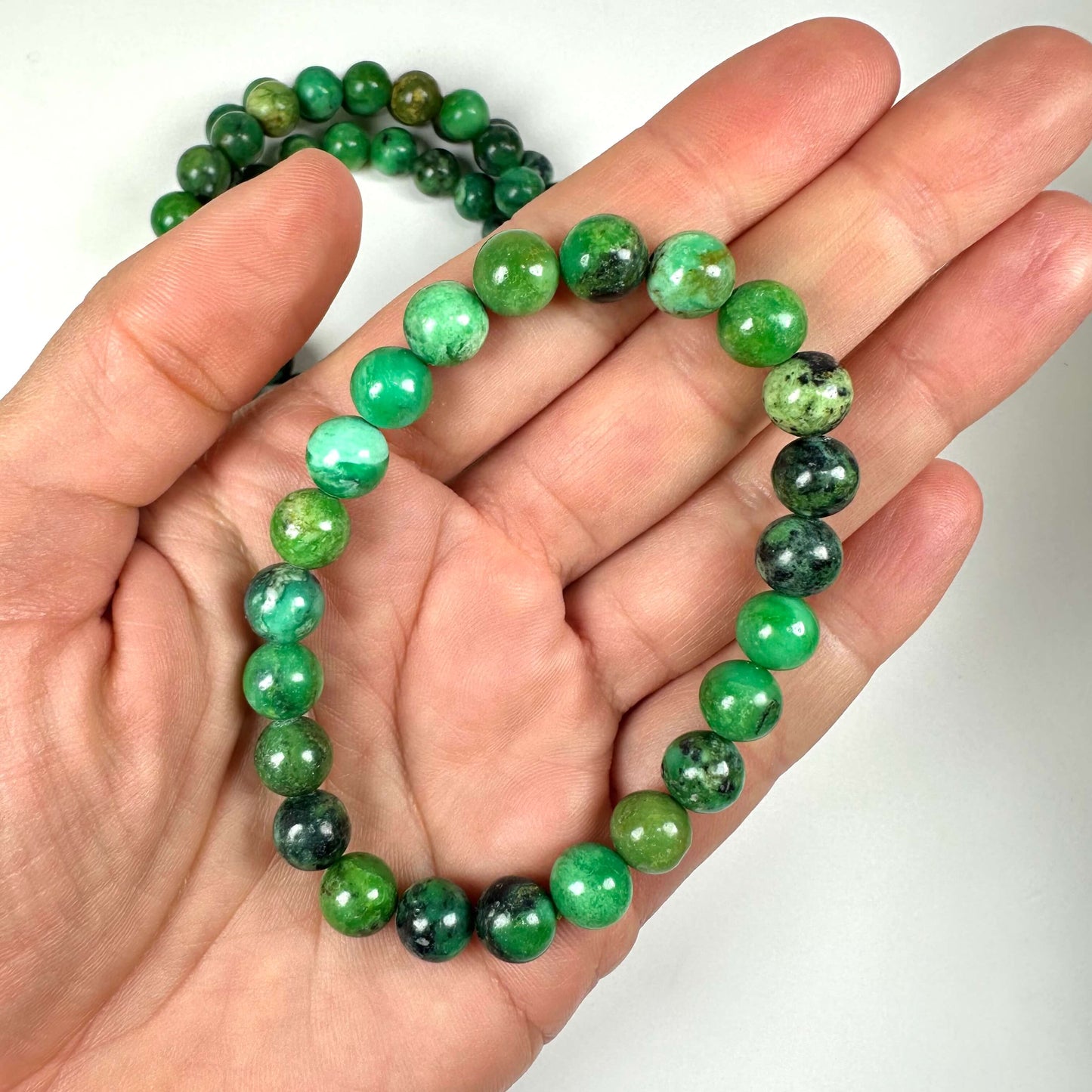 Hånd, der holder et grønt Variscit armbånd 8mm med 24 perler.