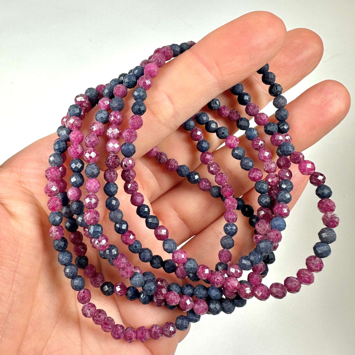 En hånd holder Rubin safir armbånd 4mm facet med lilla og blå perler.