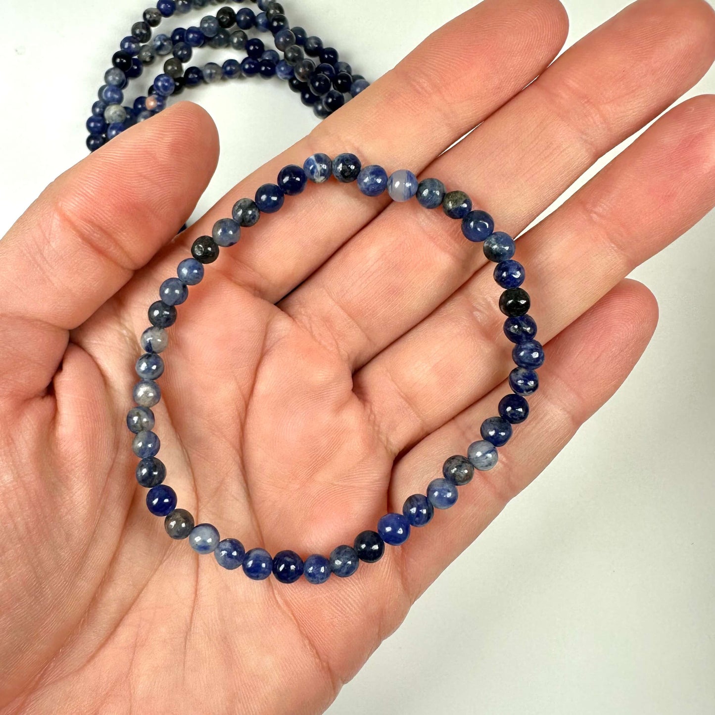 En hånd holder en blå perlehalskæde lavet af små, runde stenperler.